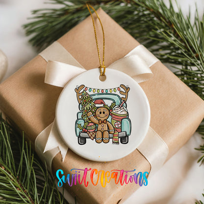 A white ceramic ornament with a gingerbread man and reindeer on a truck, surrounded by pine branches and a ribbon.