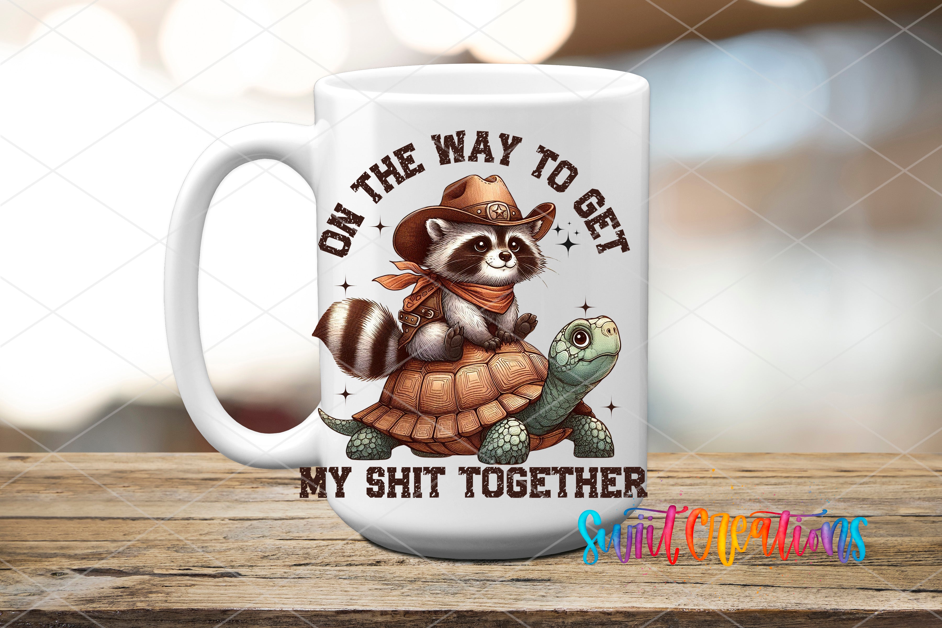 A white ceramic mug with a cartoon image of a raccoon wearing a cowboy hat and holding a turtle, along with the text "ON THE WAY TO GET MY SHIT TOGETHER" printed on it.