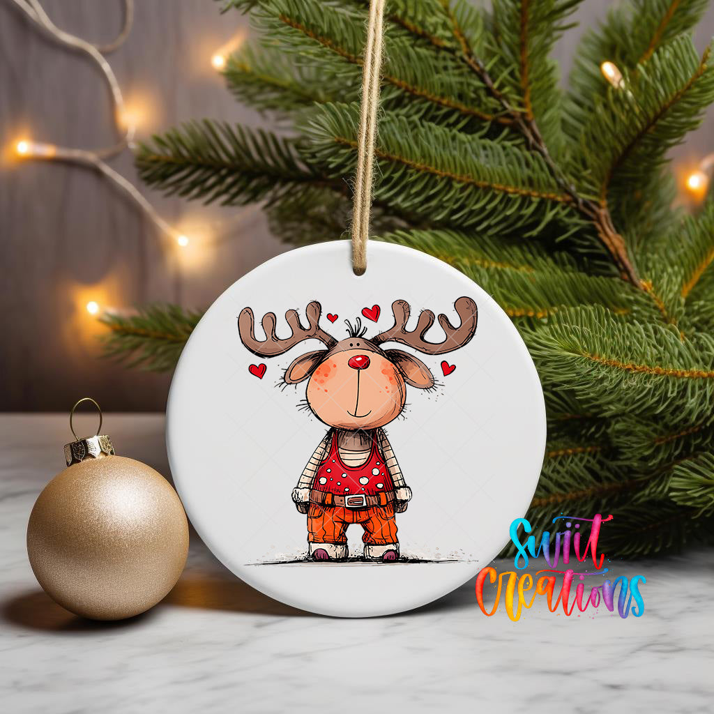 A white ceramic ornament featuring a cartoon reindeer with antlers and hearts, hanging on a string next to a gold ornament and a Christmas tree.