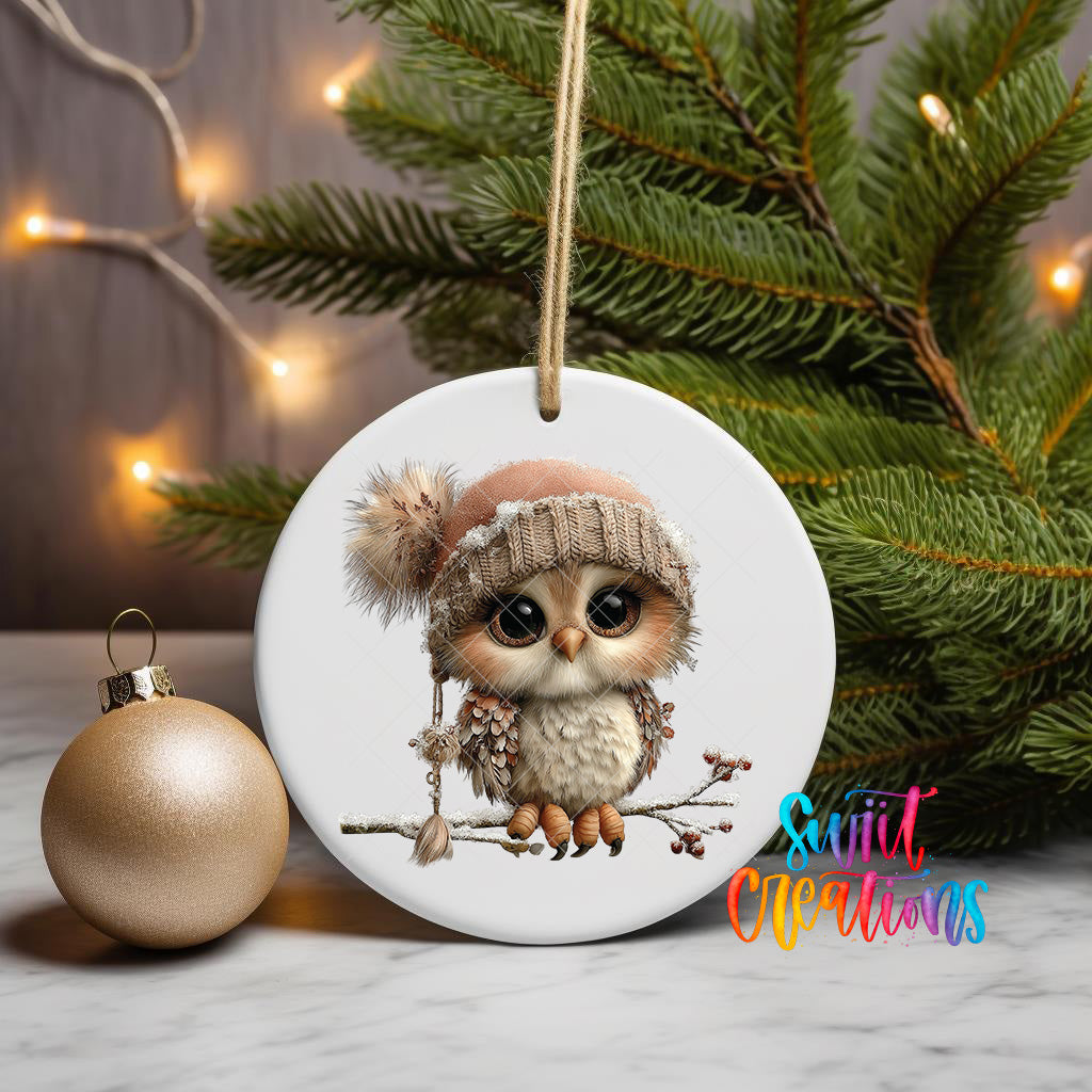 A white ceramic ornament featuring a cute owl wearing a knit hat and sitting on a branch, with a Christmas tree and twinkling lights in the background.