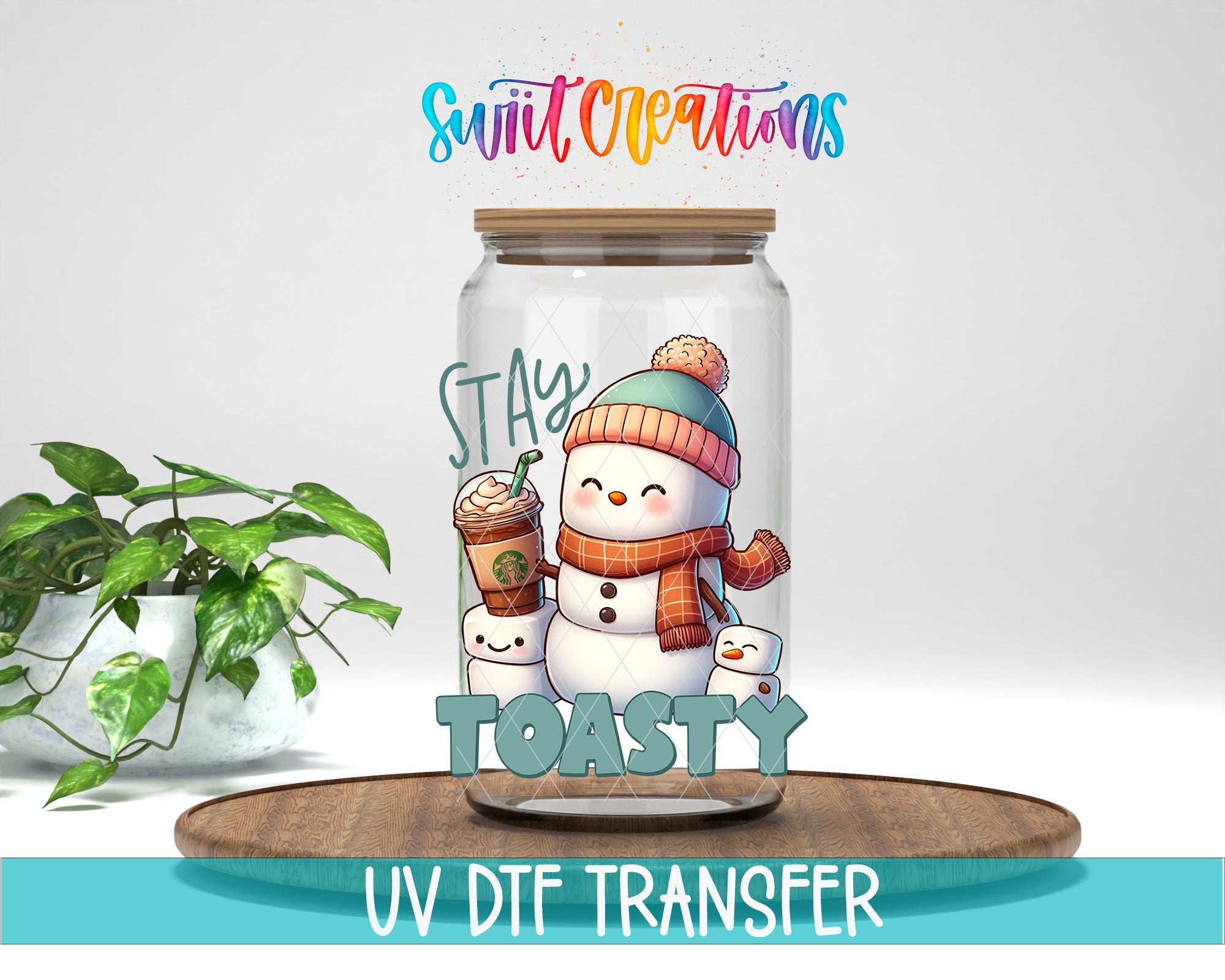 A glass jar with a snowman and a cup of coffee inside, along with the text "STAY TOASTY" and "Swift Creations" written above it. The jar is placed on a wooden surface, and there is a potted plant in the background.