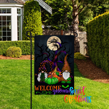 A garden sign featuring a Halloween-themed illustration of gnomes and pumpkins, with a full moon and a spooky tree in the background.