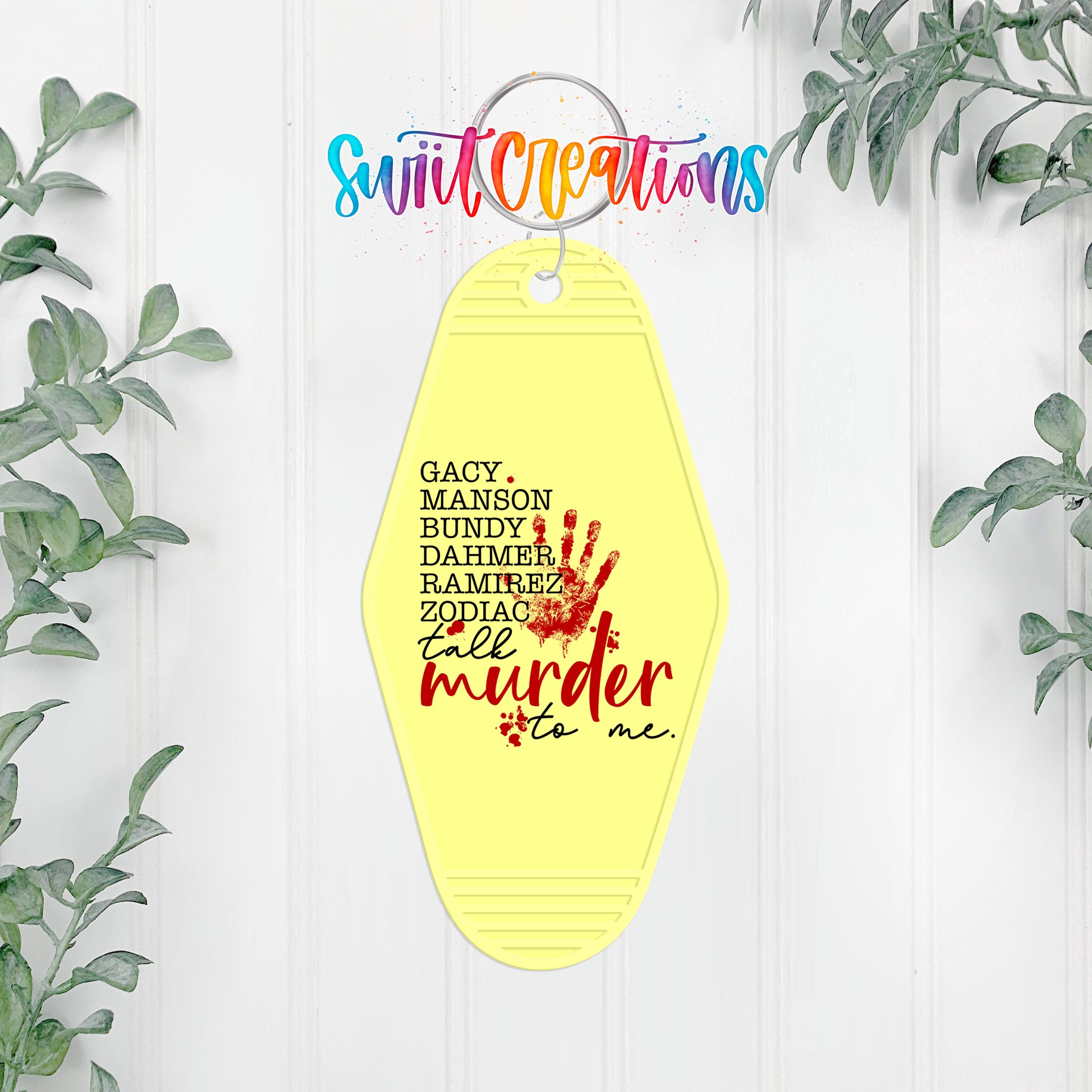 A yellow keychain with a handprint design and text on it, hanging on a white wall with greenery in the background.
