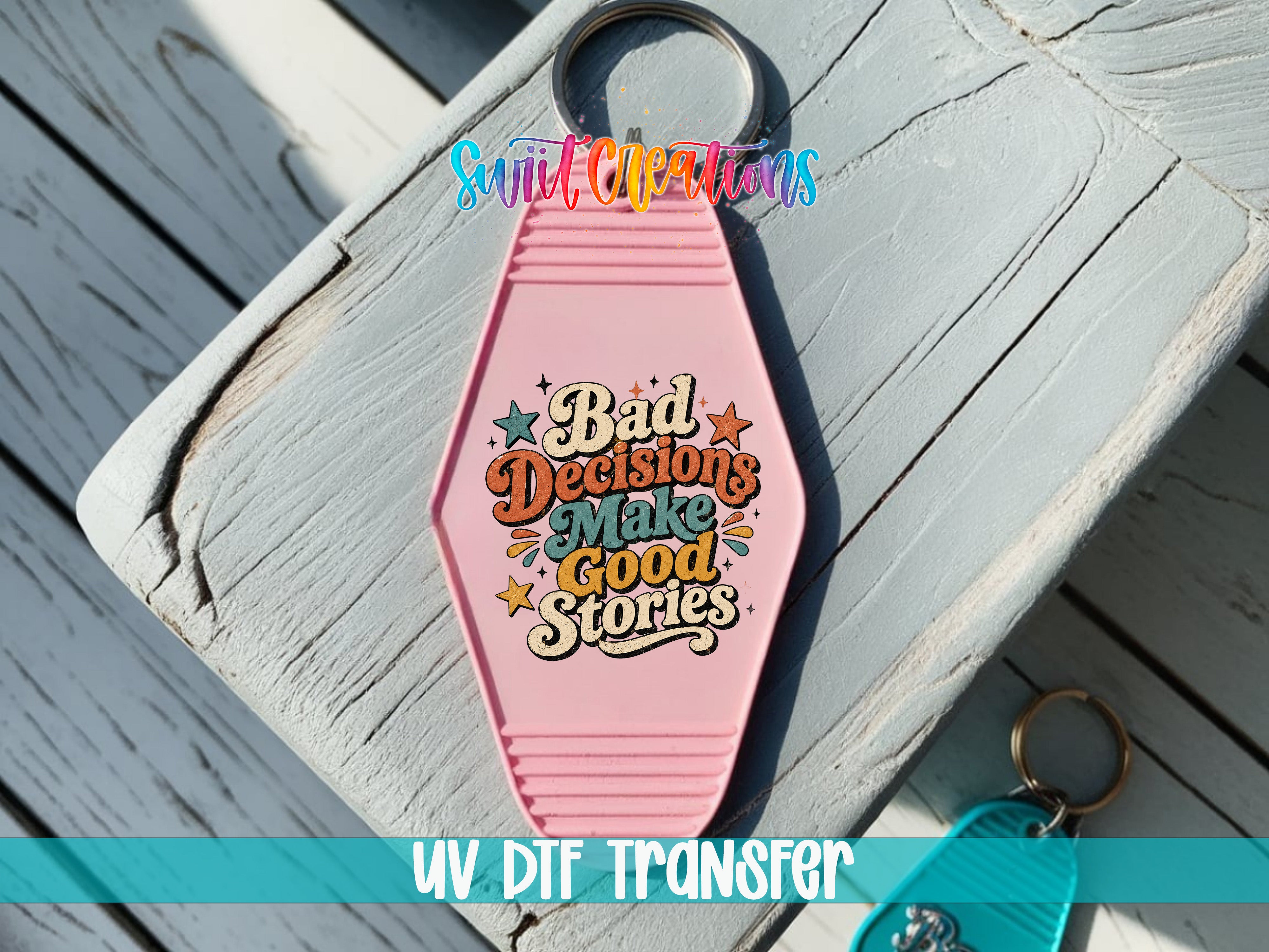 A pink keychain with a colorful design and text that says "Bad Decisions Make Good Stories" is placed on a wooden surface.