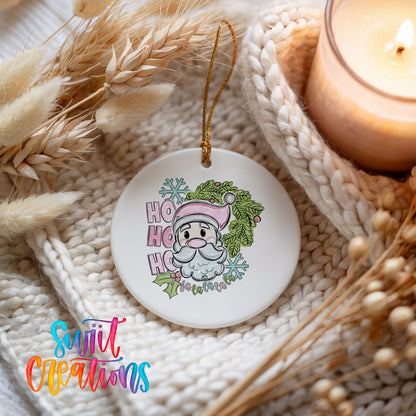 A white ceramic ornament with a Santa Claus design and the text "HOOK HOOK" is displayed on a white knitted blanket, with a lit candle in the background.