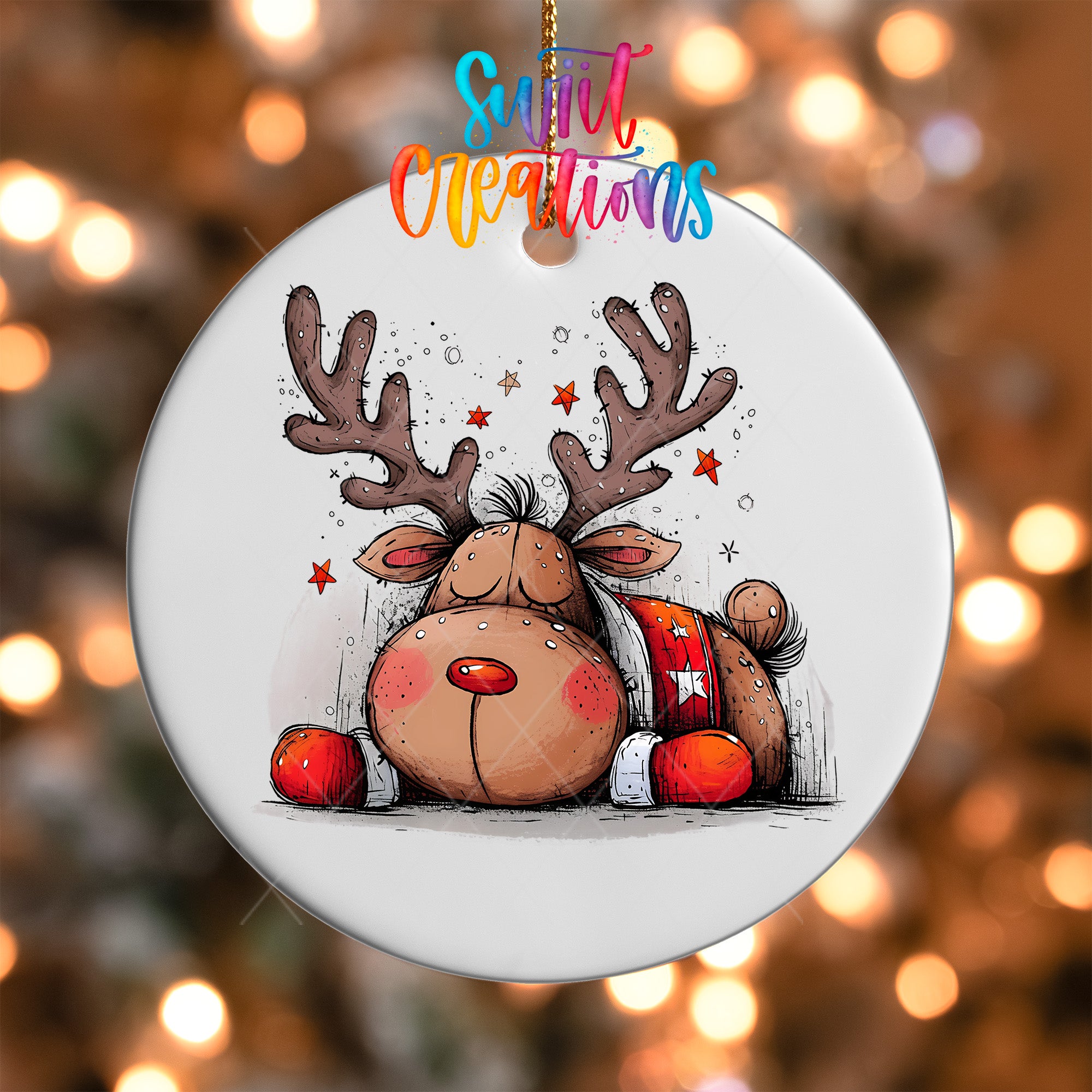 A white ornament with a cartoon illustration of a sleeping reindeer with antlers and a star on its chest, surrounded by twinkling lights.