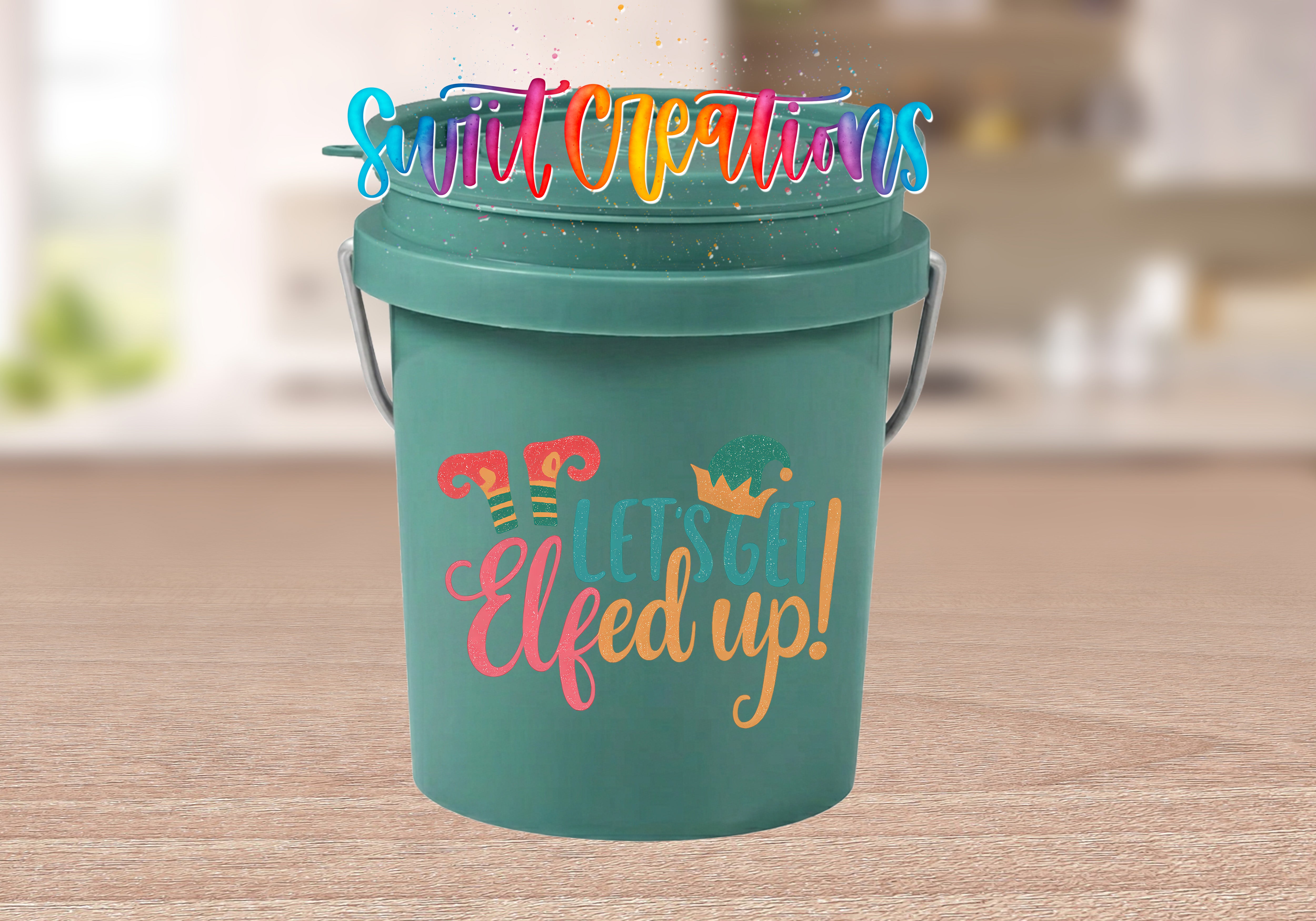 A green bucket with a colorful, whimsical design and text on it, placed on a wooden surface.