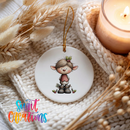 A white ceramic ornament featuring a cartoon elf with a holly leaf on its head, hanging on a white knitted blanket.