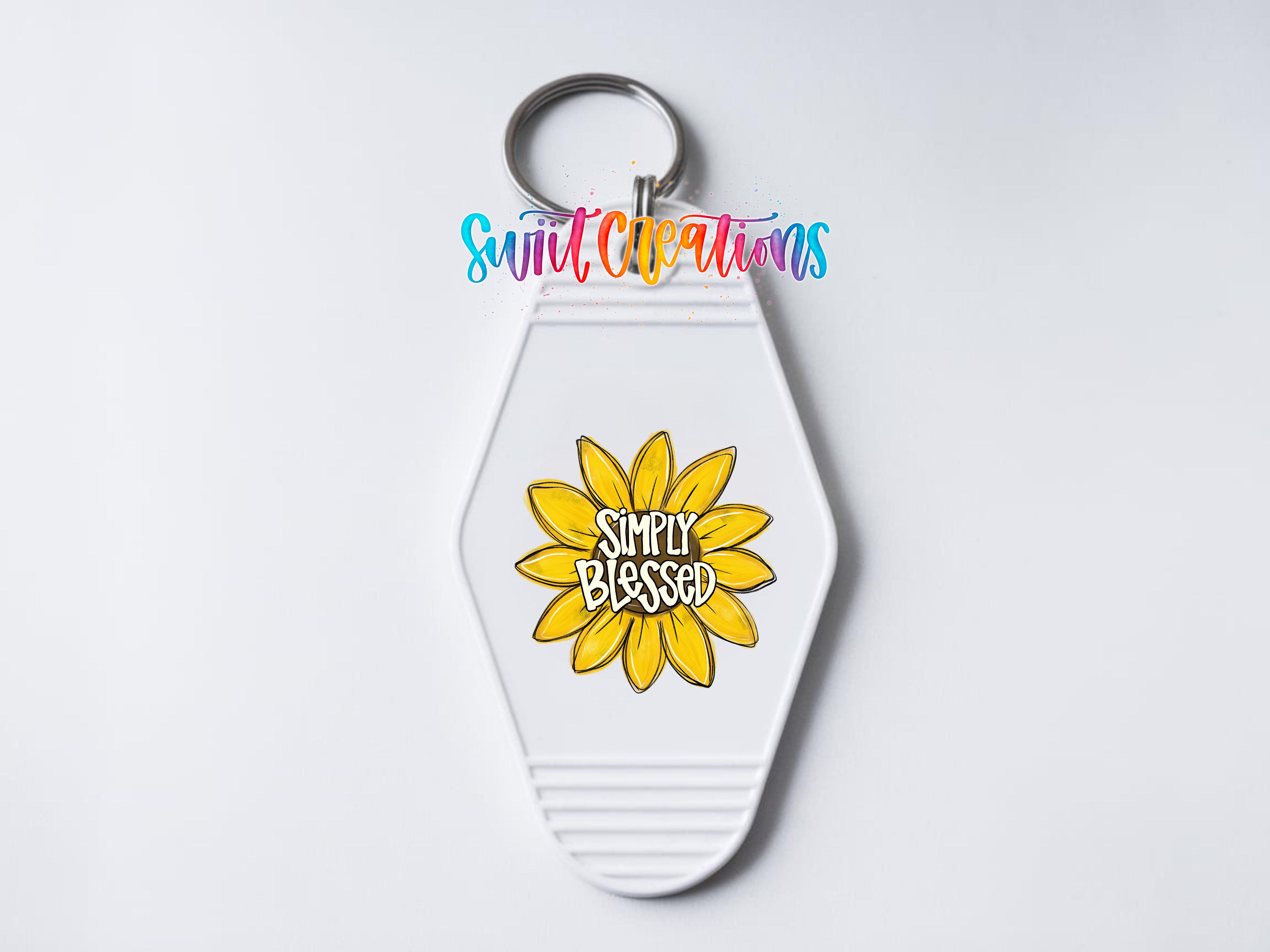 A keychain with a white hexagonal shape and a yellow flower design. The flower has the text "Simply Blessed" written on it.