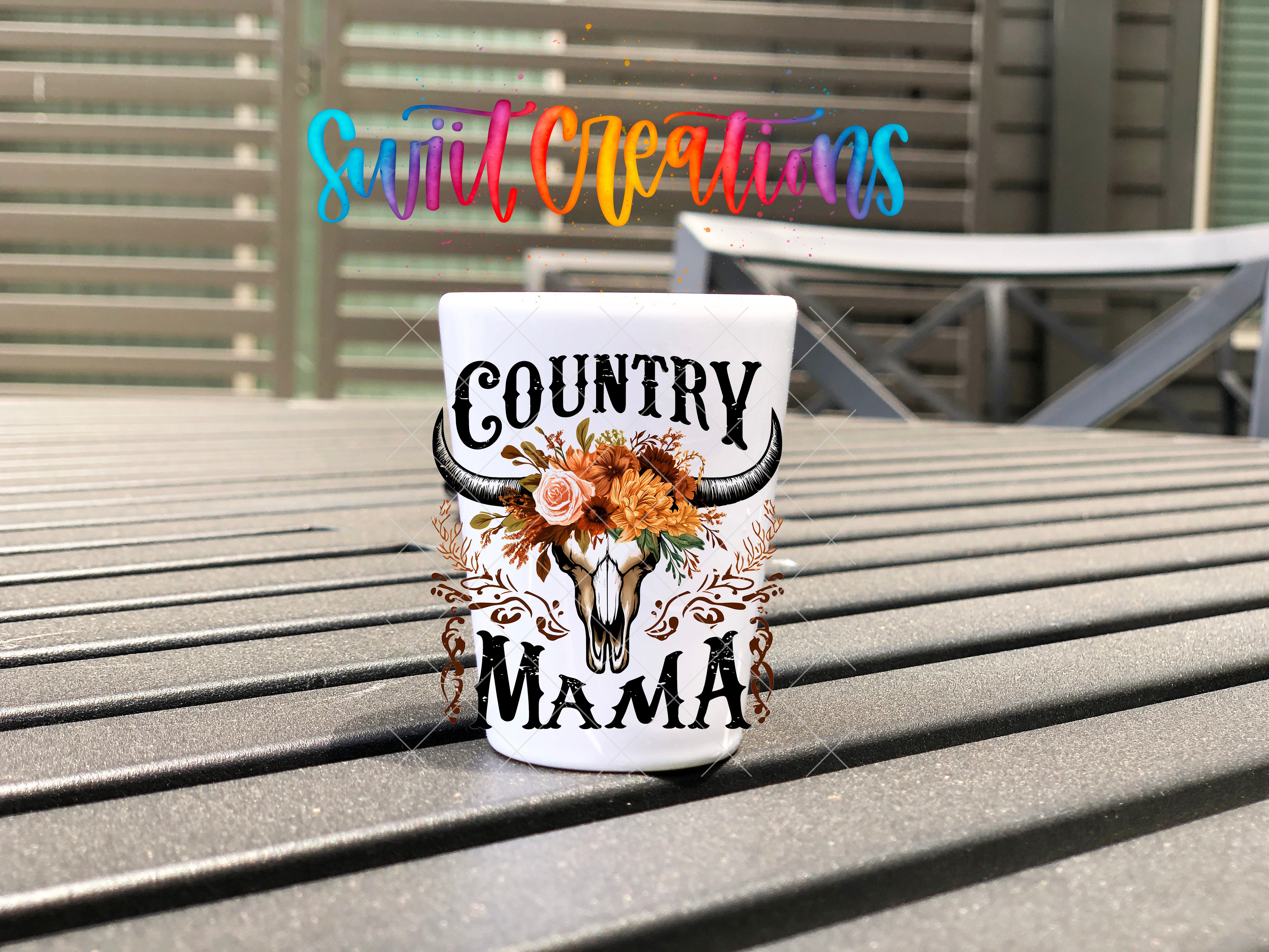 A white mug with a floral design and the text "COUNTRY MAMA" printed on it, placed on a wooden surface.