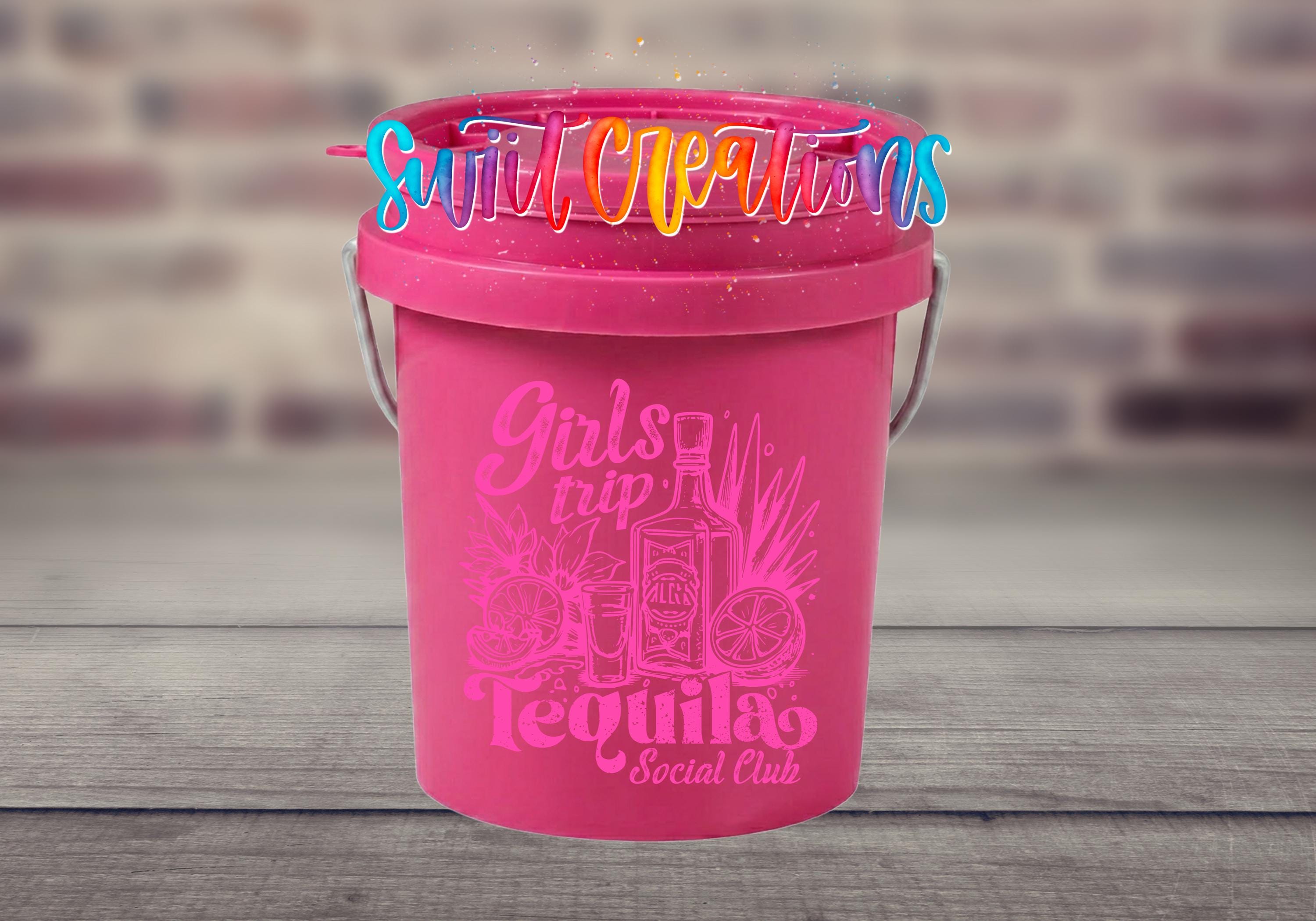 A pink bucket with a tequila-themed design and text, placed on a wooden surface against a blurred brick wall background.