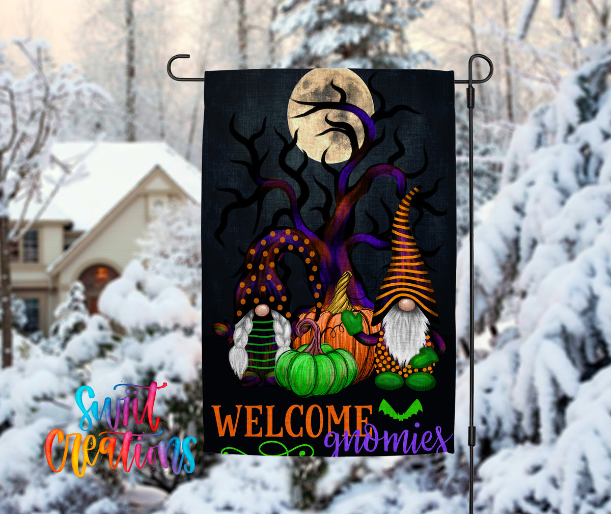 A Halloween-themed garden flag featuring gnomes and pumpkins, with a full moon in the background, is displayed in a snowy outdoor setting.