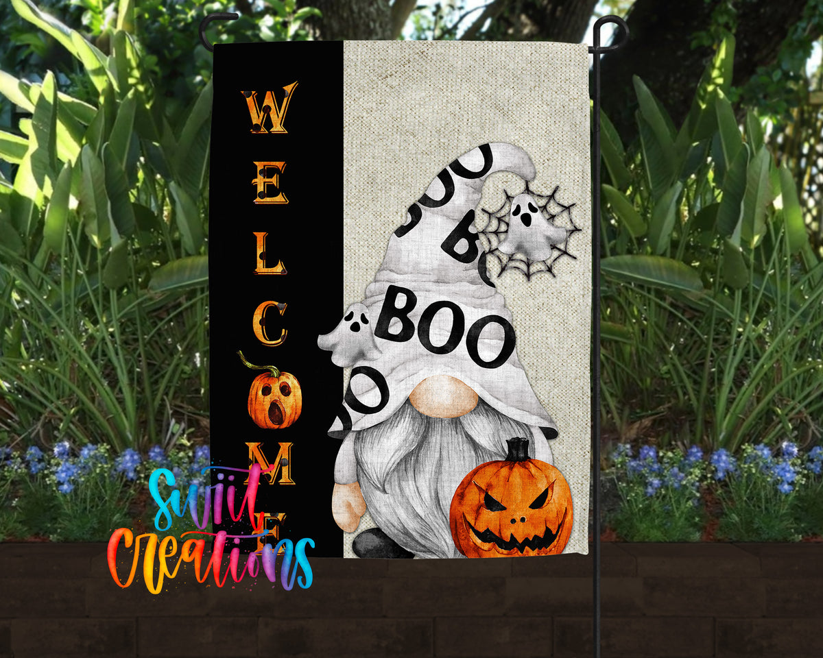 a Halloween-themed garden decoration with a gnome holding a pumpkin and a spider web. The decoration is surrounded by greenery and flowers, creating a festive atmosphere.