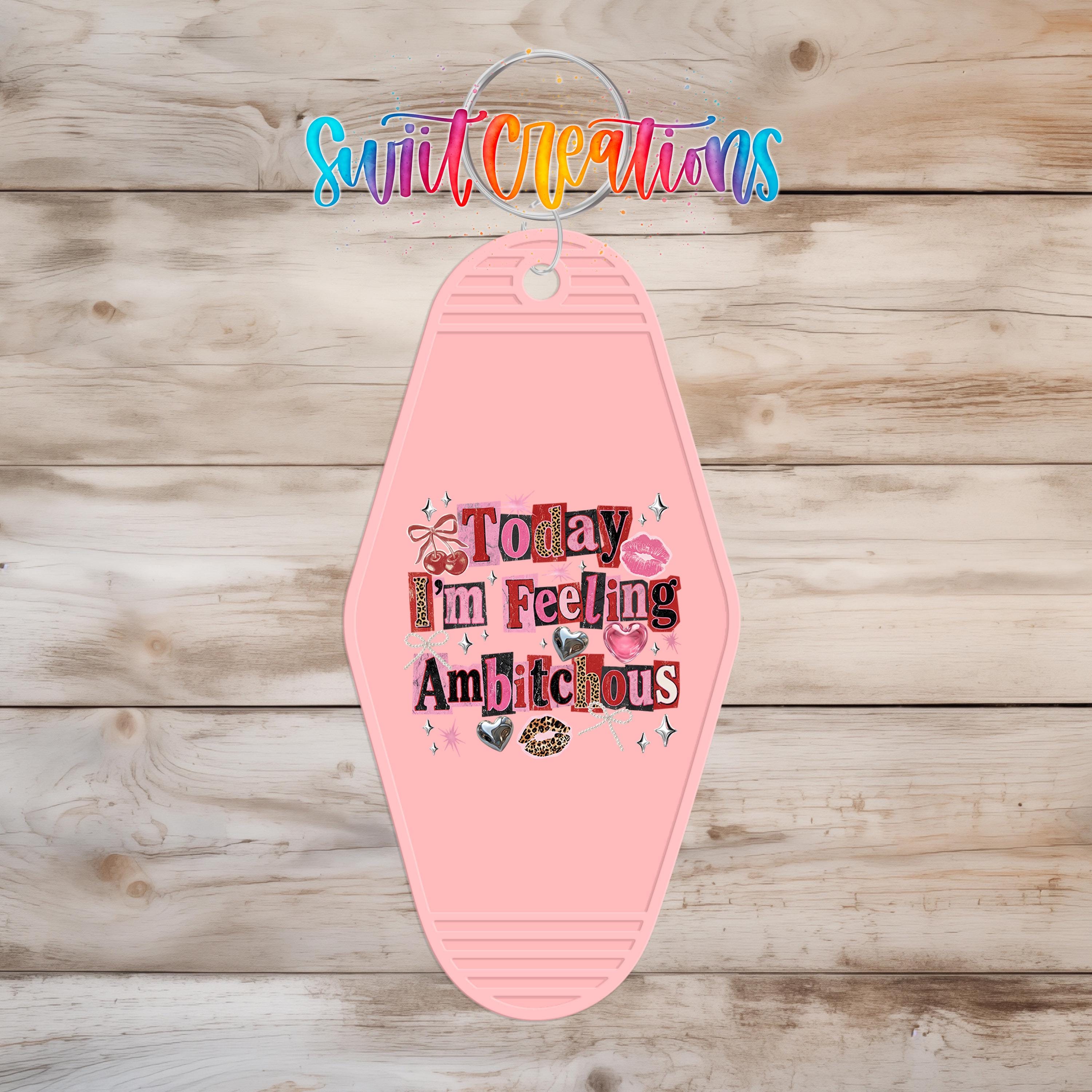 A pink keychain with text that says "Today I'm feeling ambitious" hanging on a wooden background.