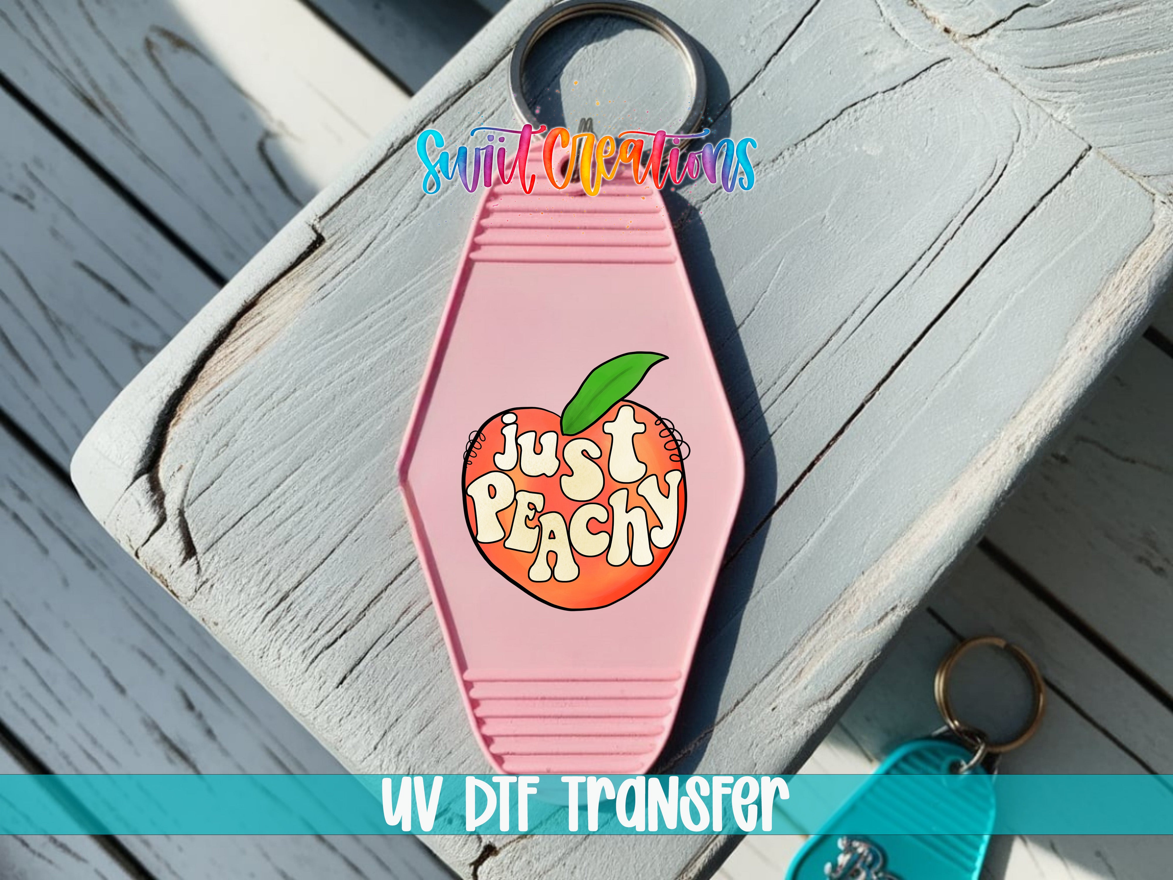 A pink keychain with a peach design and the text "Just Peachy" printed on it, placed on a wooden surface.