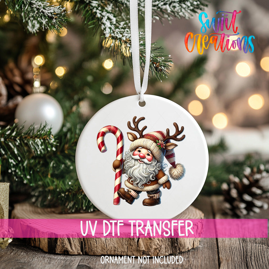 A white ornament with a Santa Claus figure and a candy cane is hanging on a Christmas tree.