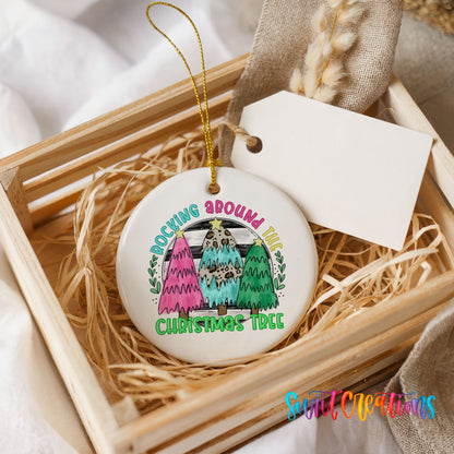 A white ceramic ornament with a colorful design of three Christmas trees, placed in a wooden crate.