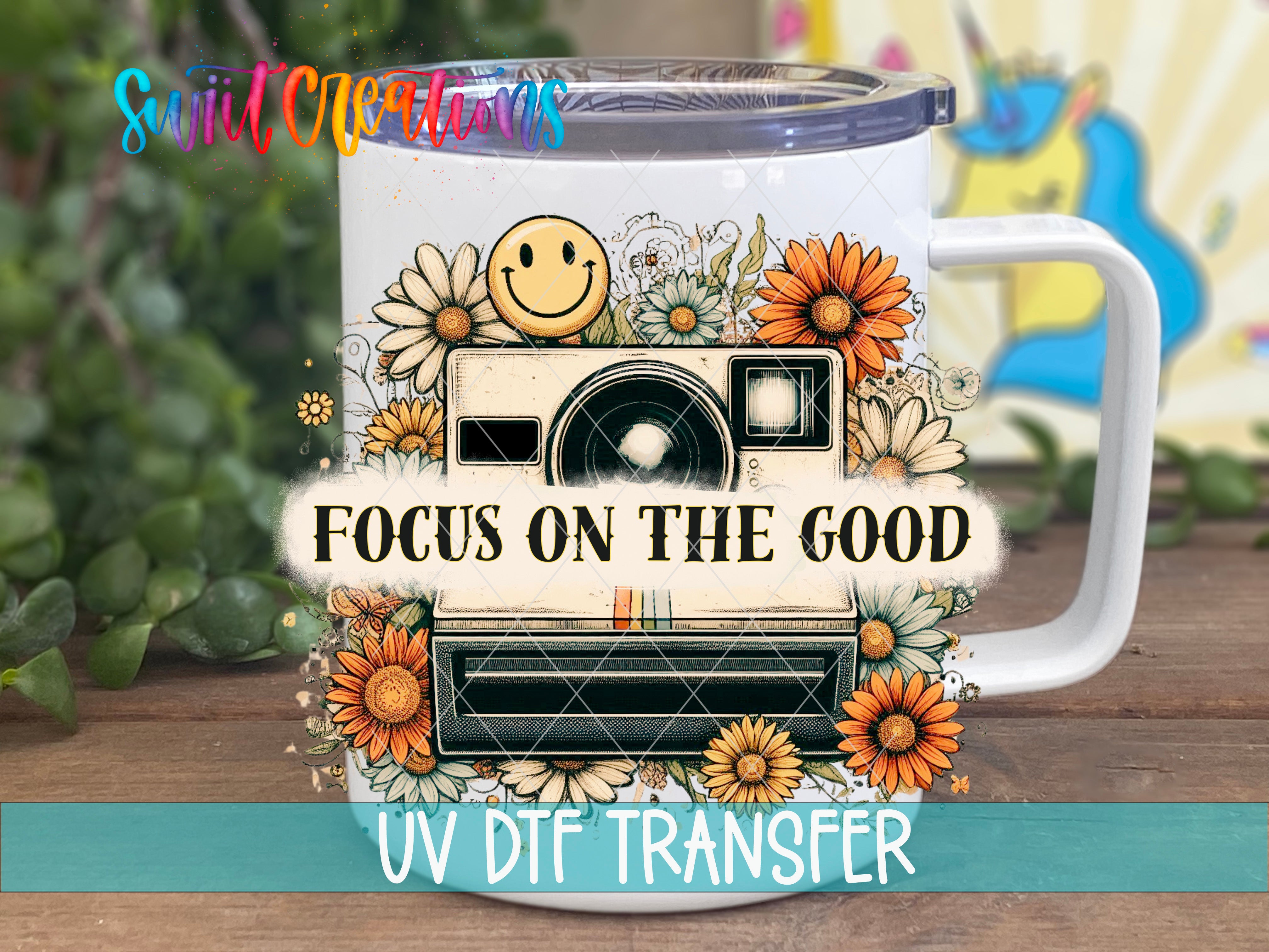 A white mug with a floral design and a camera, along with the text "Focus on the good" and "UV DFT Transfer".