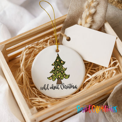 A white ceramic ornament with a leopard print design and the text "wild about Christmas" is displayed in a wooden crate, surrounded by straw.