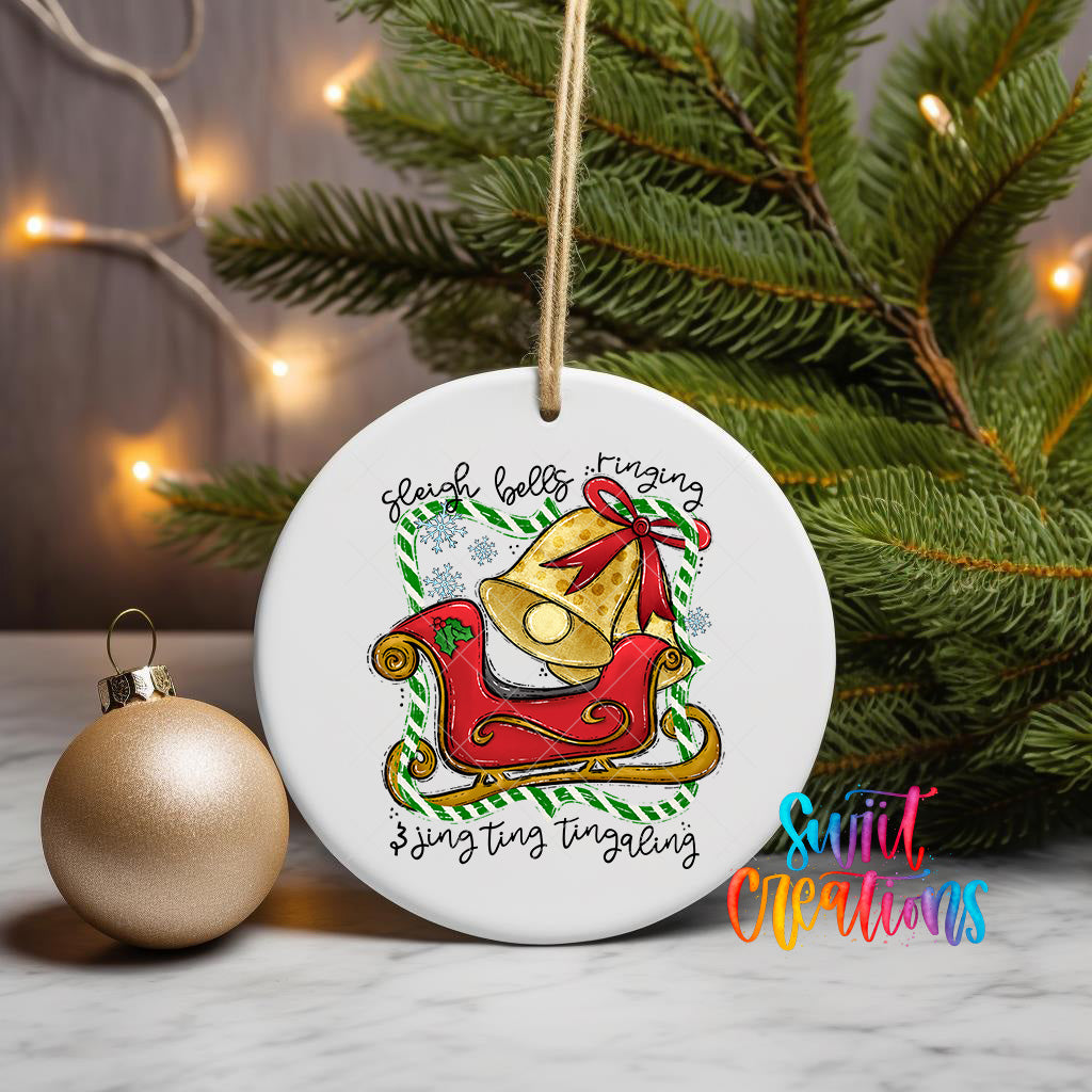 A white ceramic ornament with a Christmas tree in the background, featuring a bell and the text "Sleigh bells ringing" and "singing singing".
