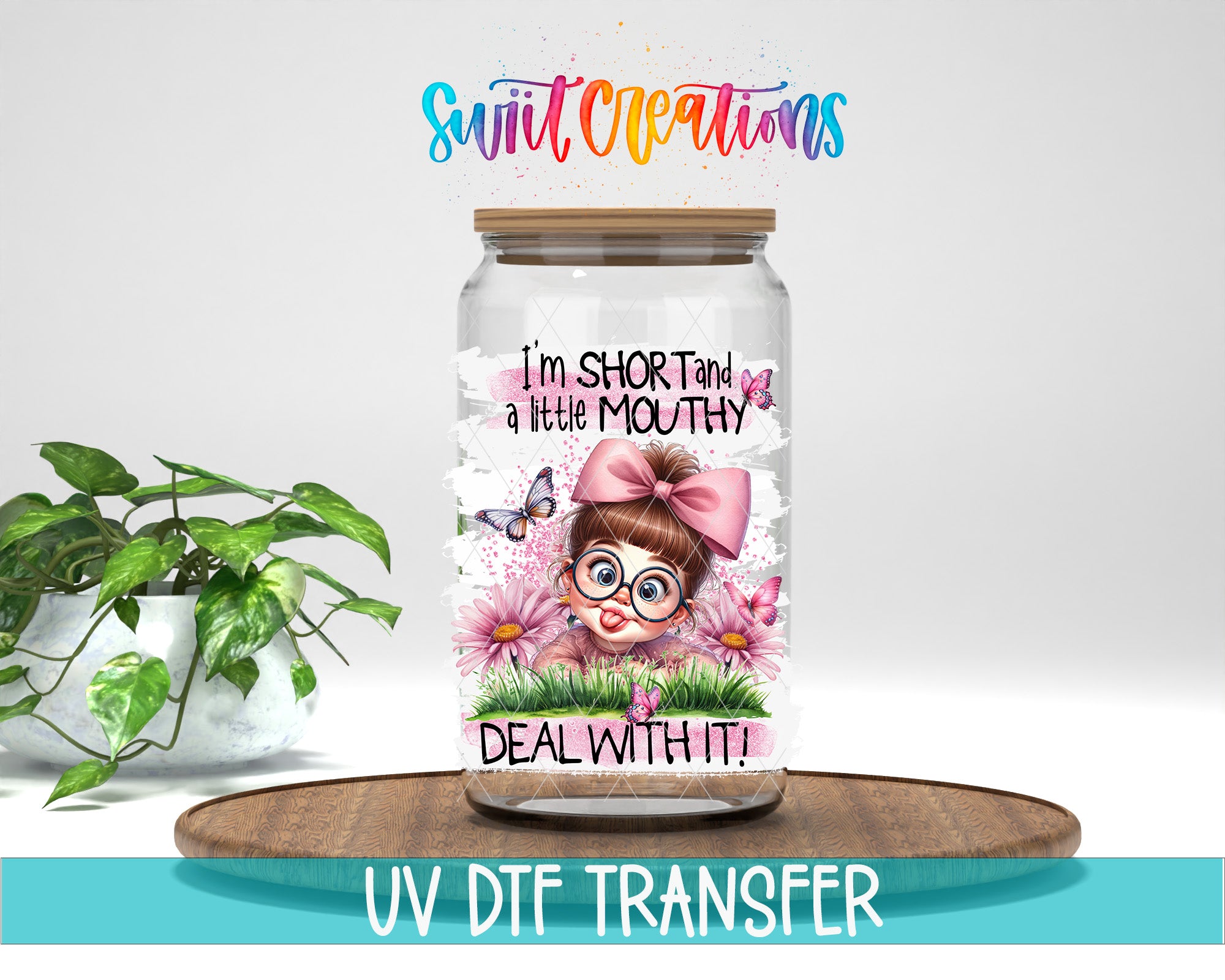 A glass jar with a cartoon girl and flowers on it, along with text that says "I'm short and a little mouthy, deal with it!" The jar is placed on a wooden surface, and there is a potted plant in the background.