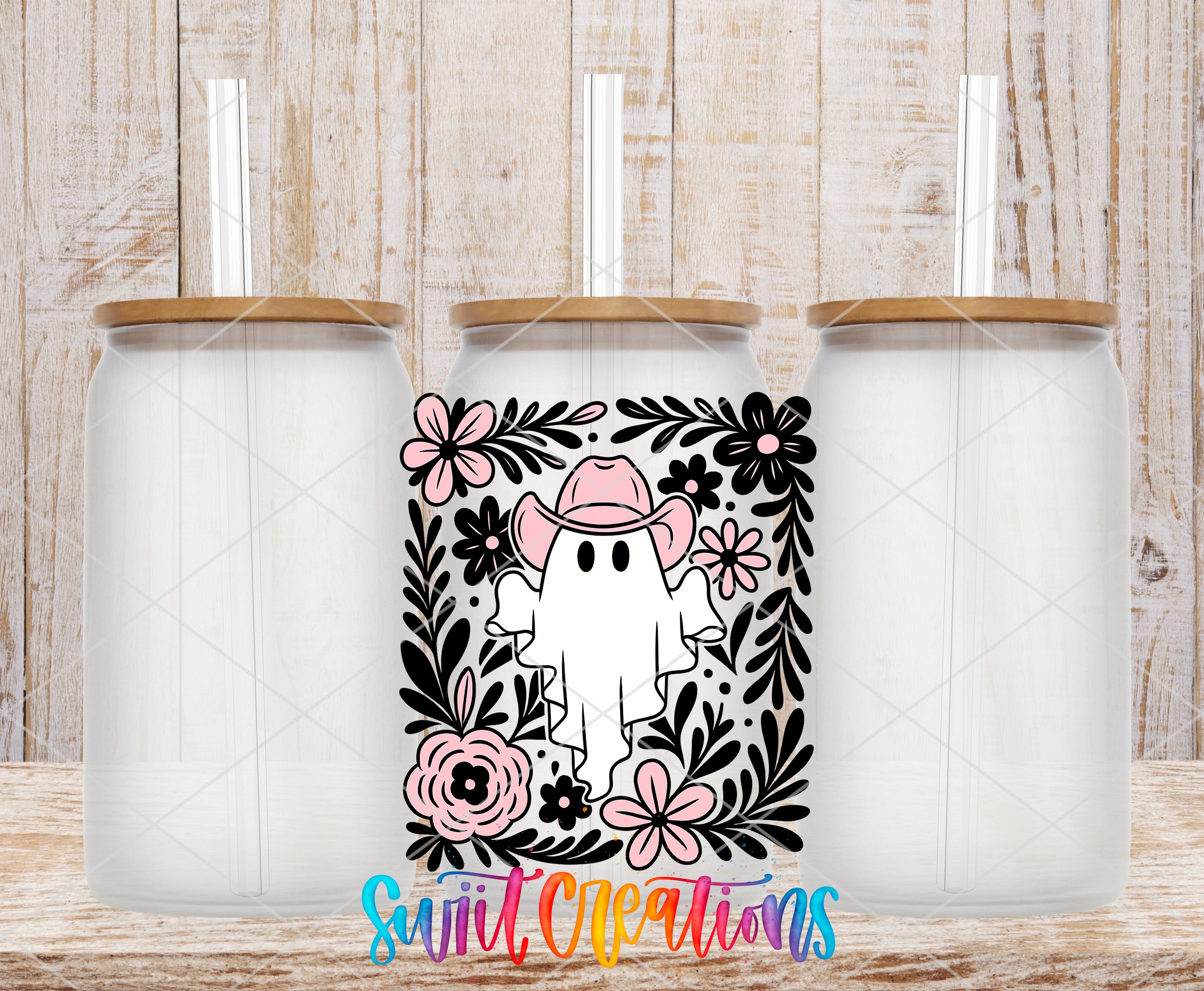 three clear glass jars with lids, each containing a straw. The jars are arranged in a row, with the middle jar having a unique design on it. The design includes a ghost wearing a cowboy hat and surrounded by flowers and leaves. The background of the image is a wooden wall with a textured appearance.