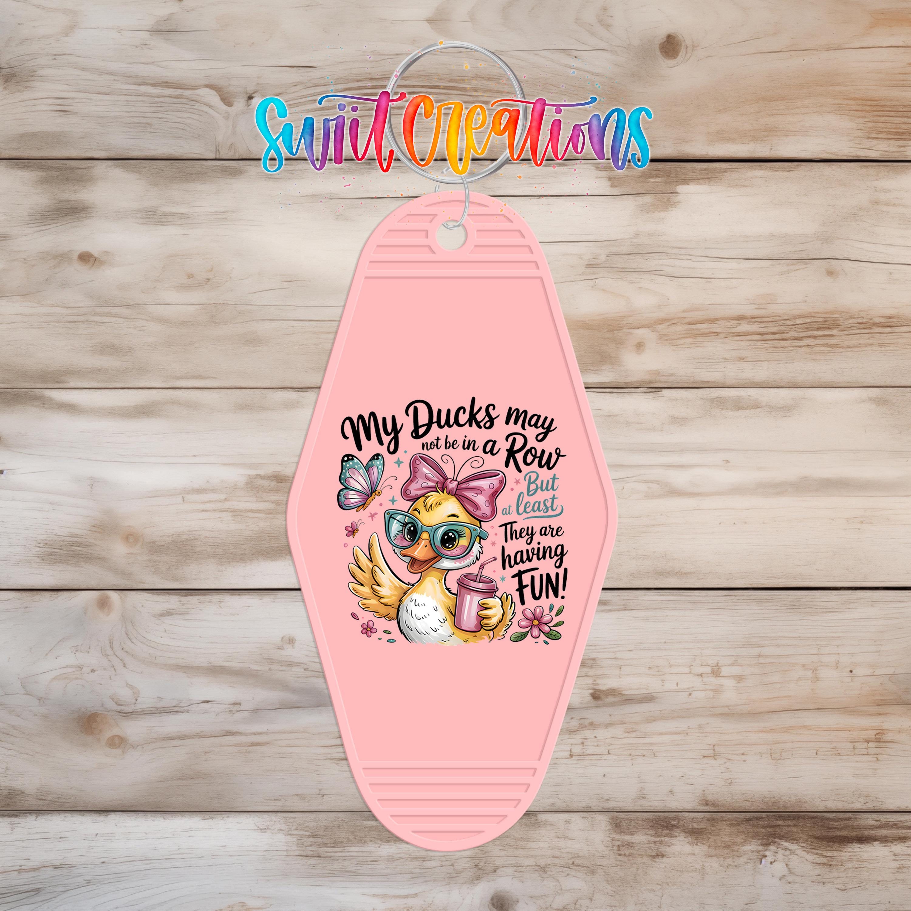 A pink keychain with a cartoon duck and text that says "My ducks may be in a row, but they are having fun!"