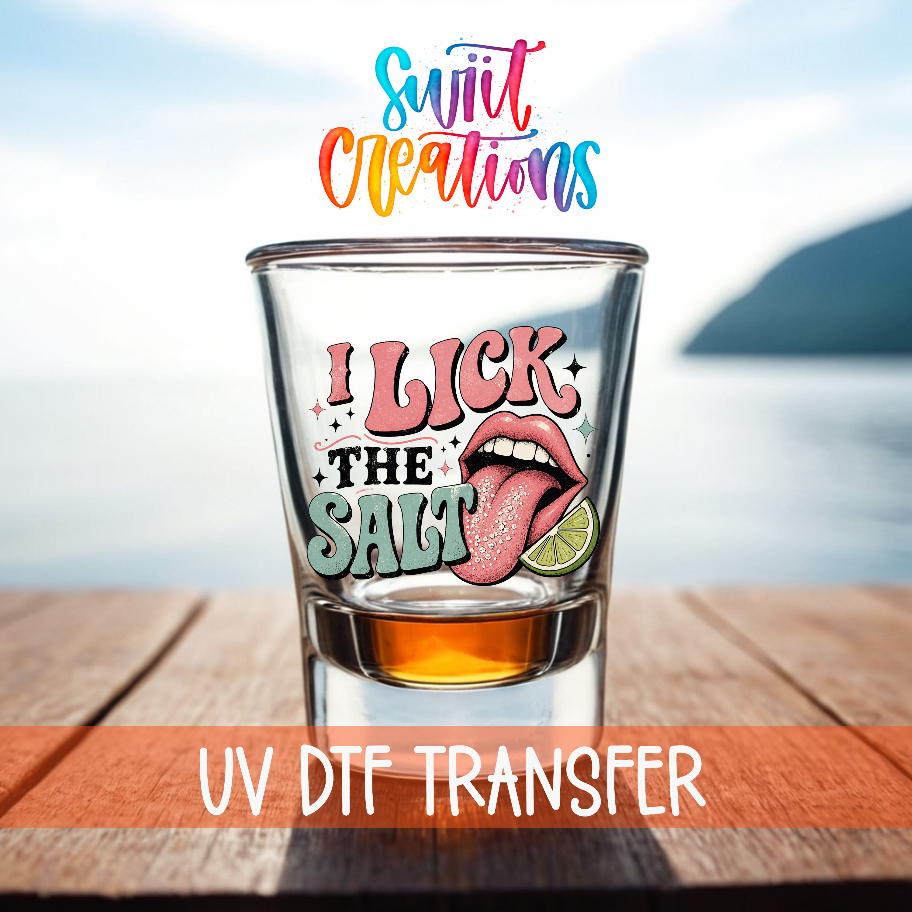 A shot glass with a colorful graphic and text on it, placed on a wooden surface with a body of water in the background.