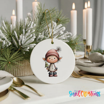 A white ornament featuring a cartoon elf holding a Christmas tree is displayed on a table, surrounded by candles and greenery.