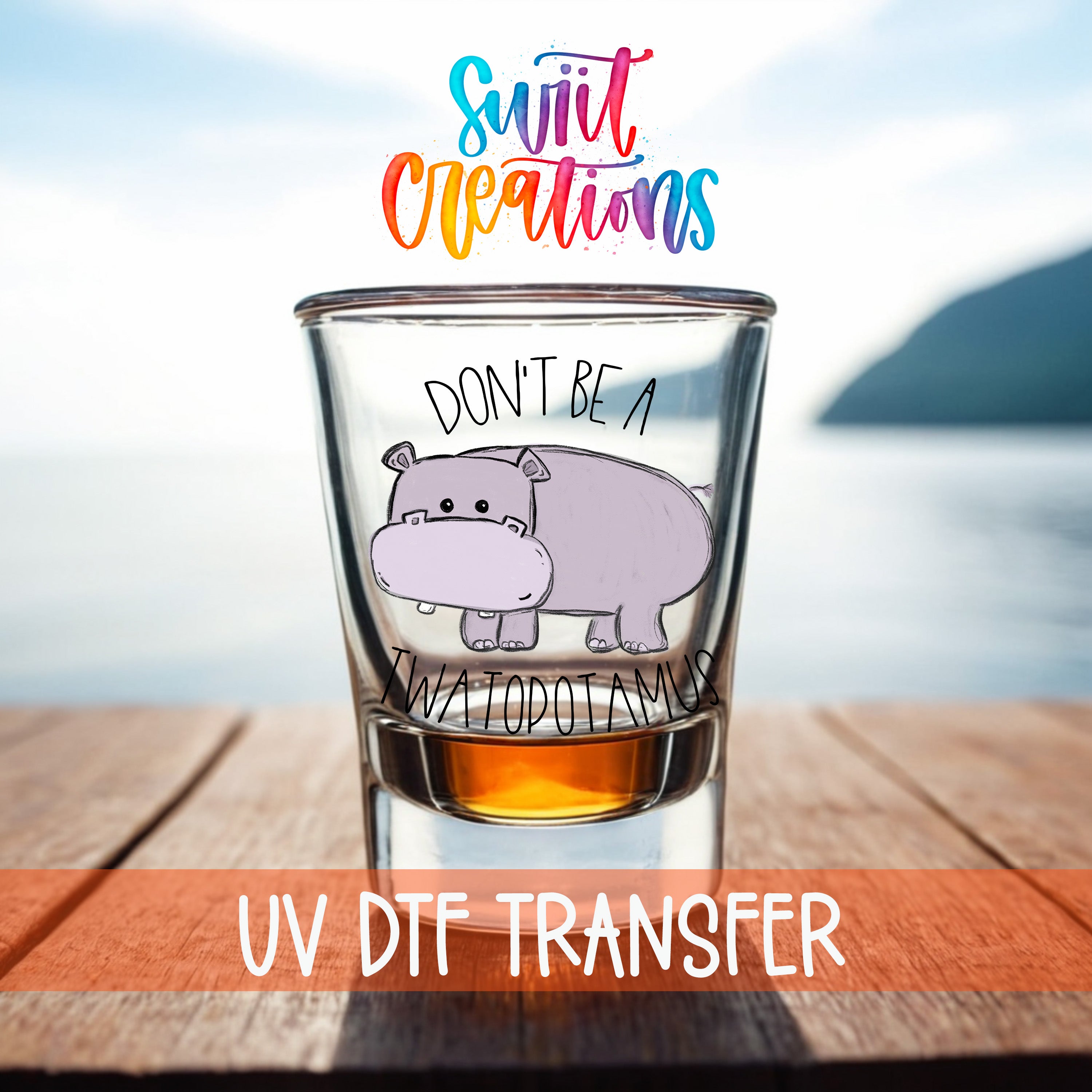 a shot glass with a cartoon hippopotamus and the text "Don't be a Swatopotamus" printed on it. The shot glass is placed on a wooden surface, with a body of water visible in the background.