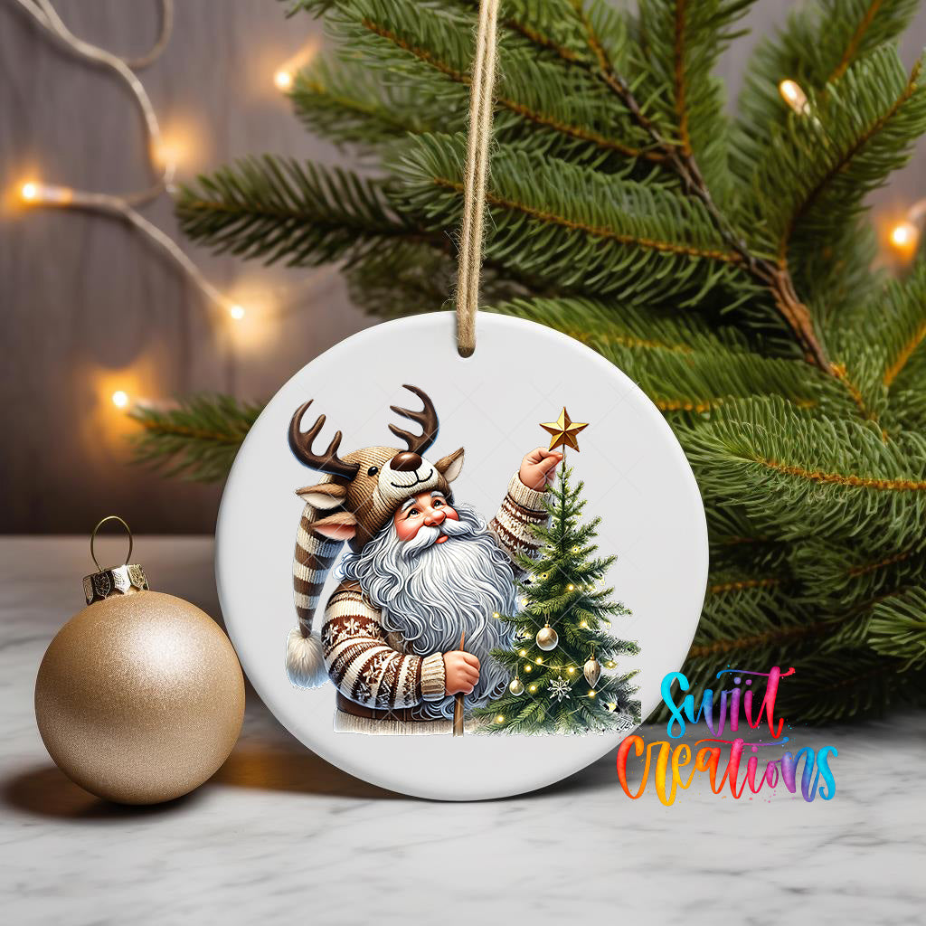 A white ceramic ornament featuring a Santa Claus figure with antlers and a star, surrounded by a Christmas tree and ornaments, including a gold ornament.