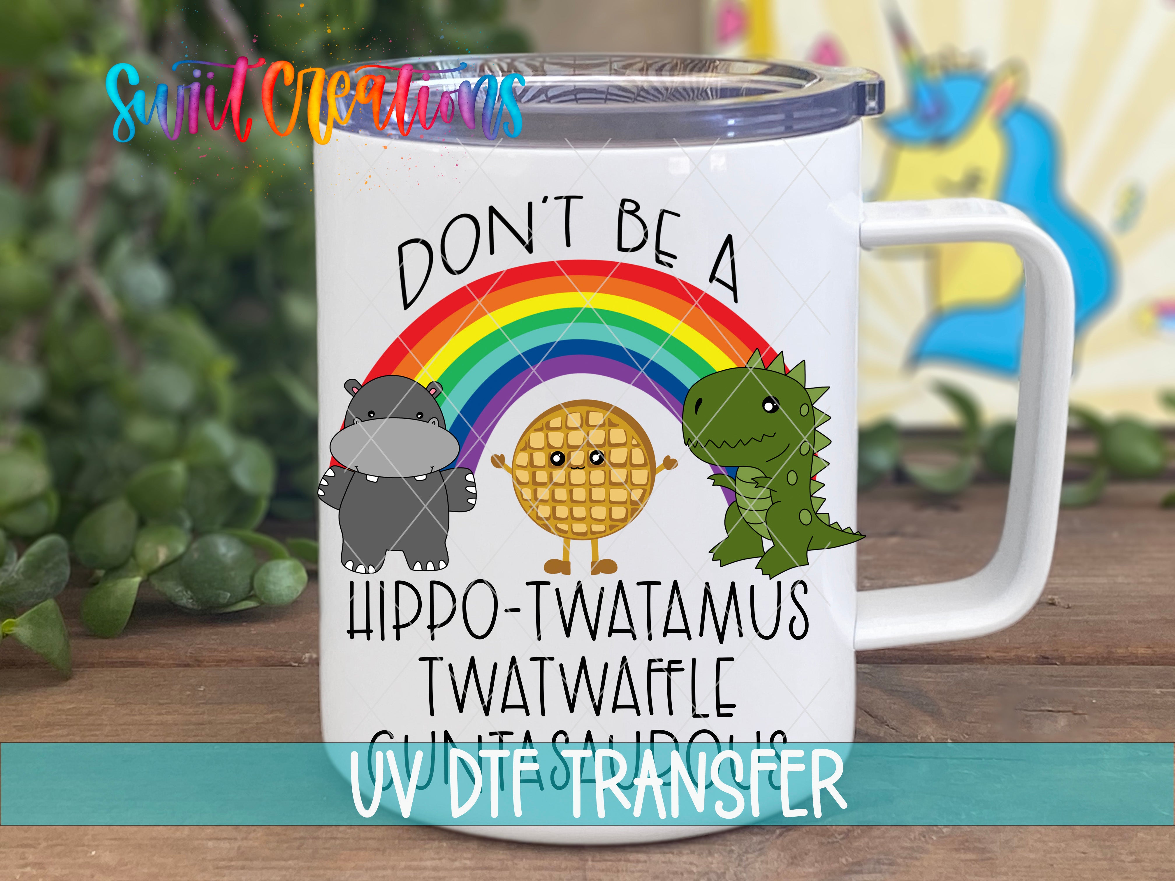 A white mug with a colorful design featuring a rainbow, a hippopotamus, a dinosaur, and a waffle. The text on the mug reads "DON'T BE A HIPPO-TWATAMUS TWATWAFLE GUNTA-HORDS".