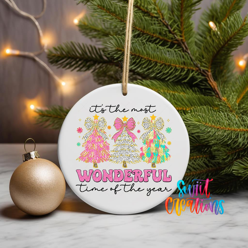 A white ceramic ornament with a festive design hangs on a Christmas tree, surrounded by twinkling lights.