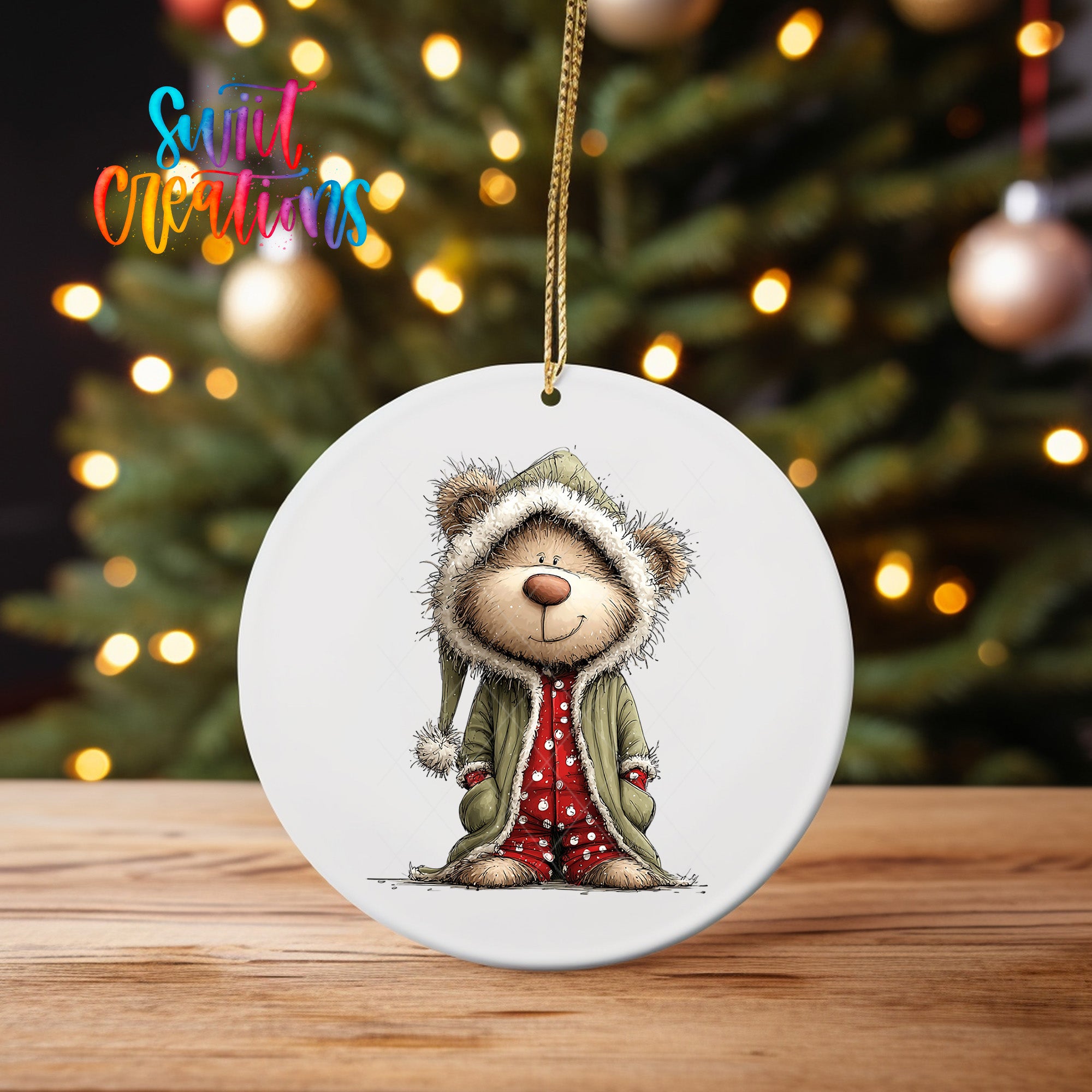 A white oval ornament featuring a cartoon illustration of a bear wearing a green coat and red polka dot pants, standing in front of a Christmas tree with twinkling lights.