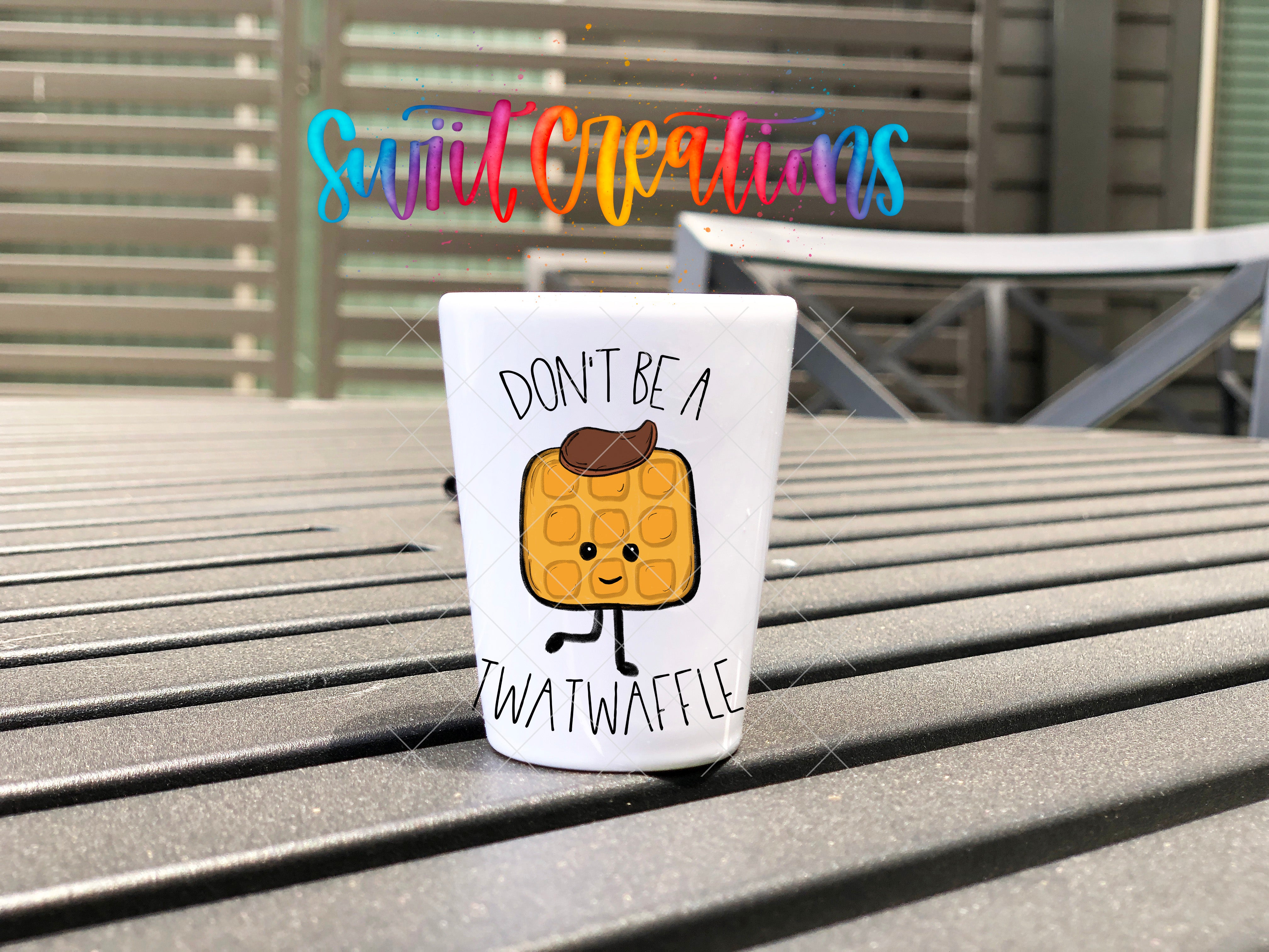 A white mug with a cartoon waffle on it, placed on a wooden surface. The mug has a message printed on it that says "Don't be a Waffle".