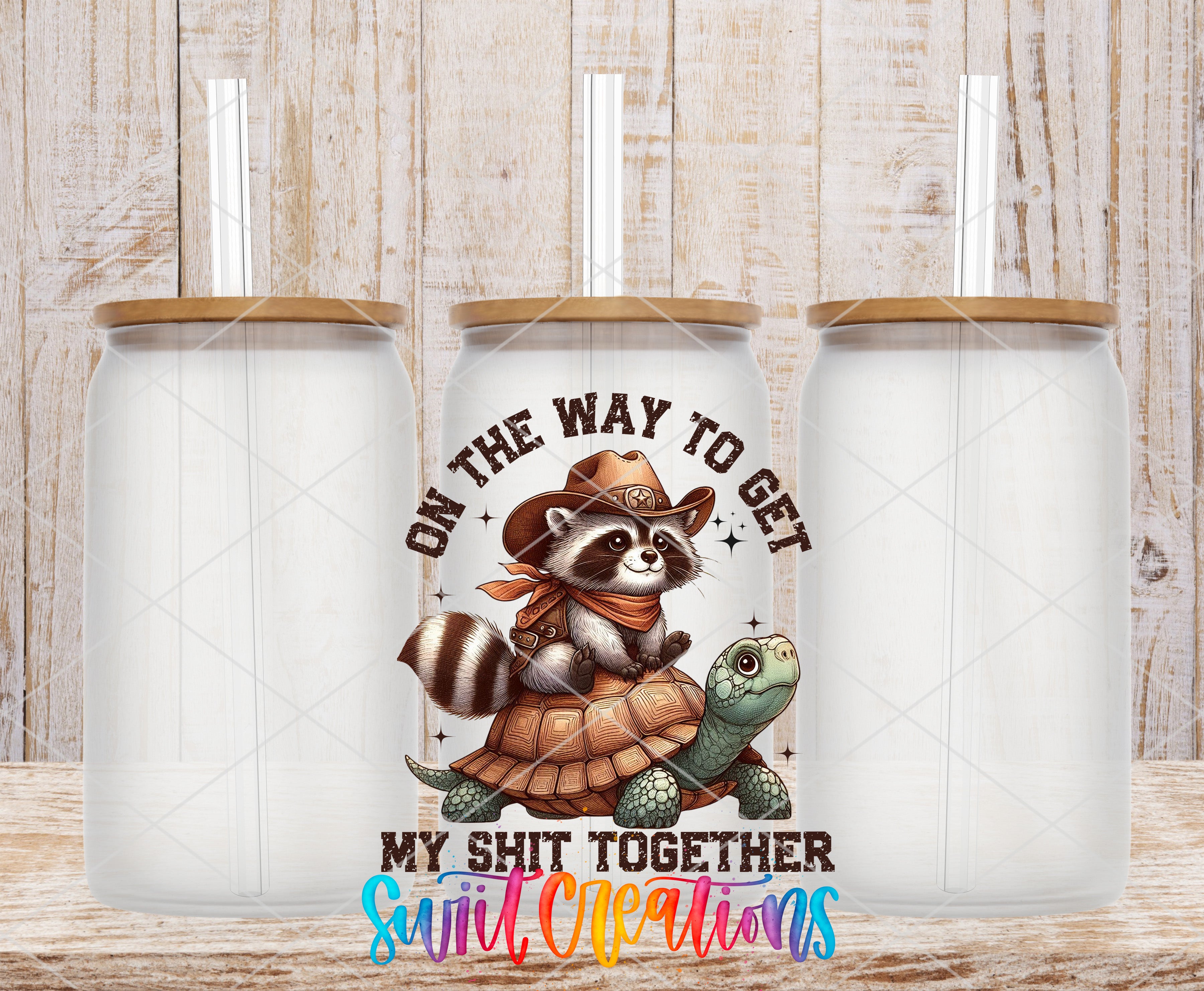 a ceramic mug with a cartoon raccoon wearing a cowboy hat and holding a turtle, along with the text "ON THE WAY TO GET MY SHIT TOGETHER" and "Suit, Creations" printed on it.