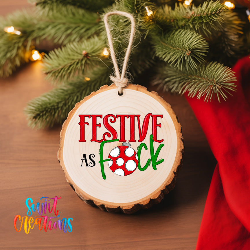 A wooden ornament with the text "FESTIVE AS FOCK" hanging on a Christmas tree, surrounded by pine branches and twinkling lights.
