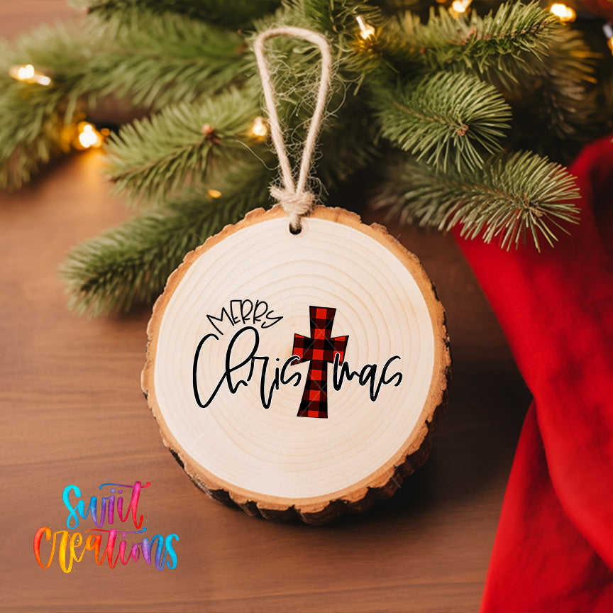 A round wooden ornament with the text "Merry Christmas" and a red and black plaid cross design hangs on a Christmas tree.