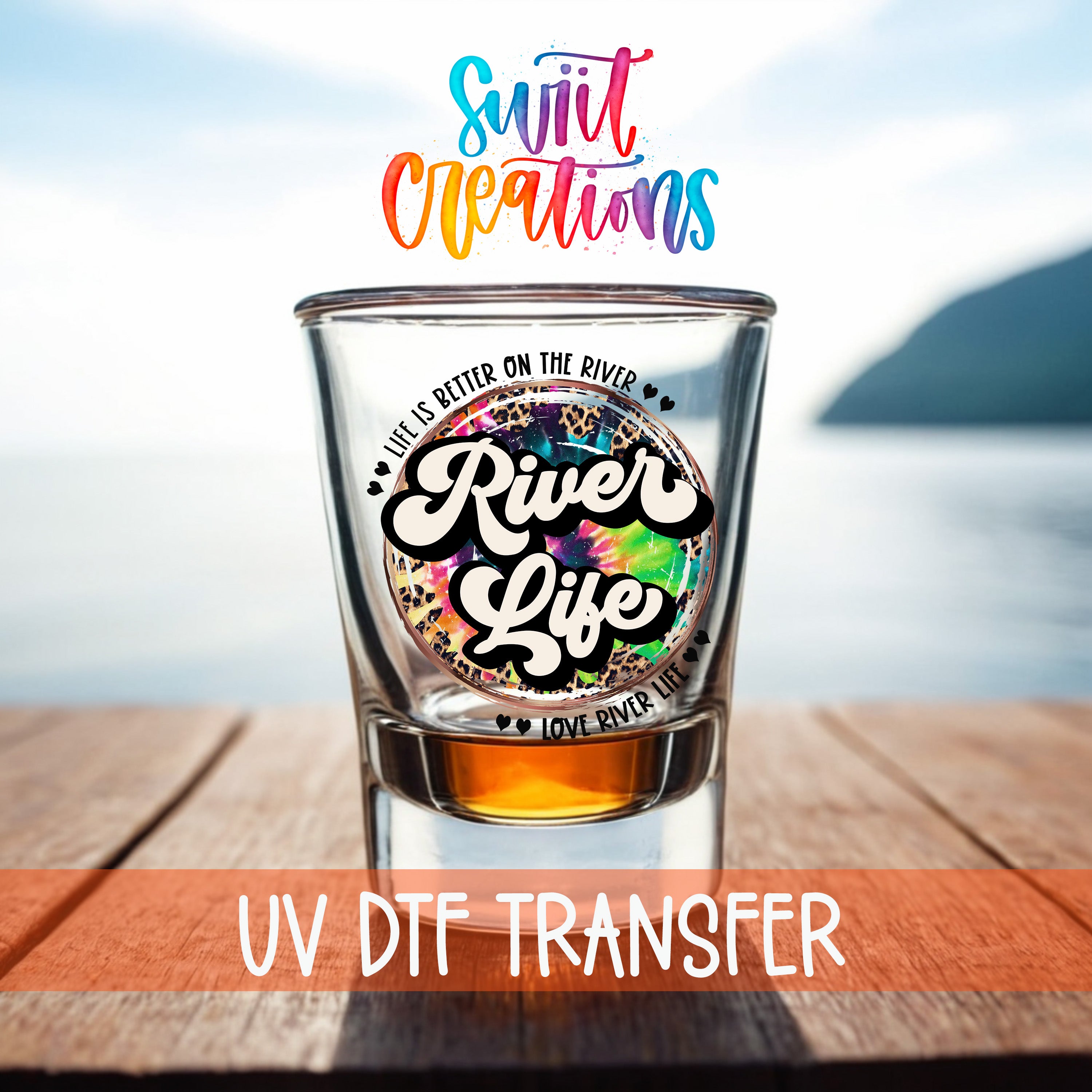 a shot glass with a colorful design and text, placed on a wooden surface with a body of water in the background.