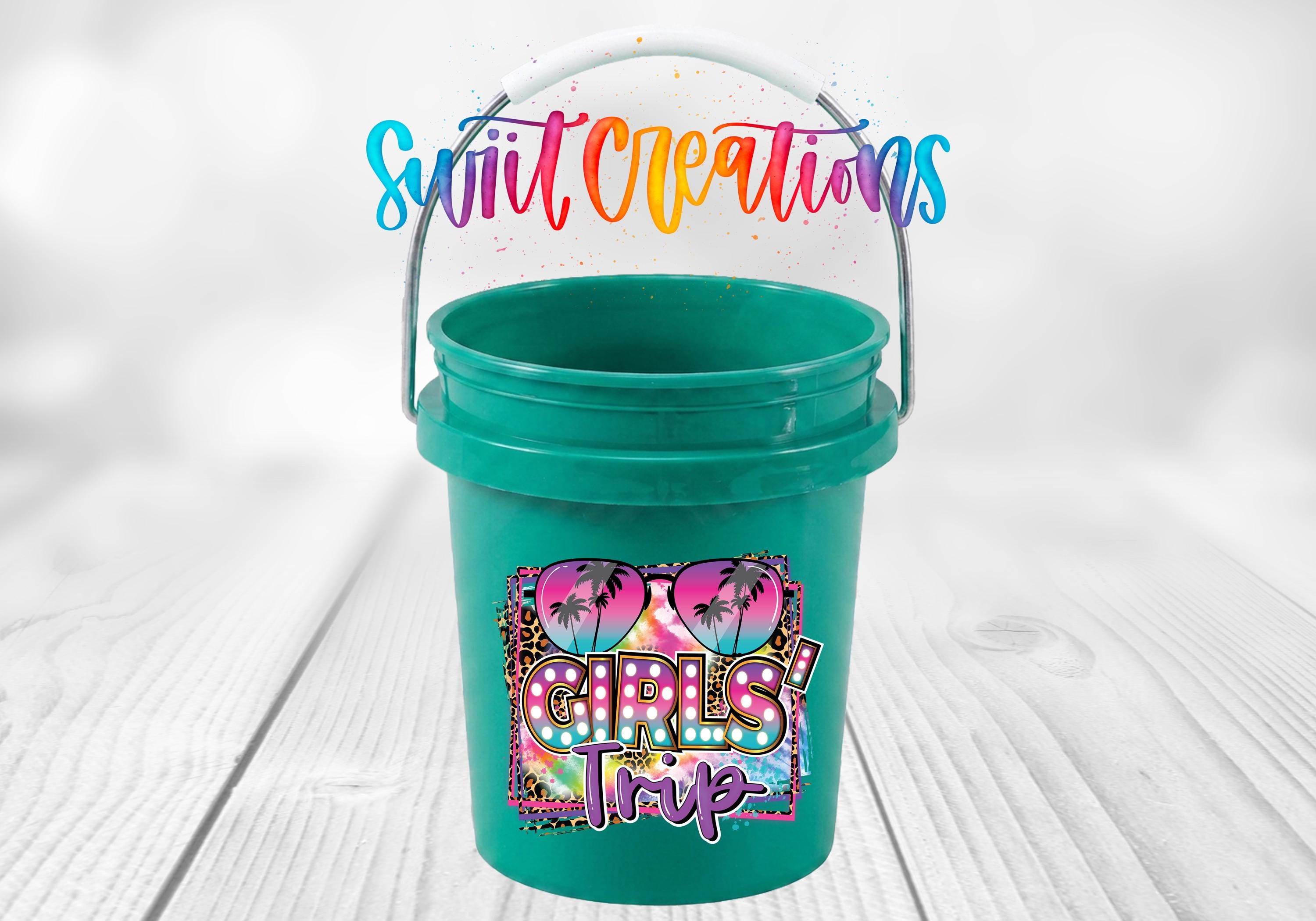 A green bucket with a colorful, tropical-themed design and text printed on it, placed on a wooden surface.