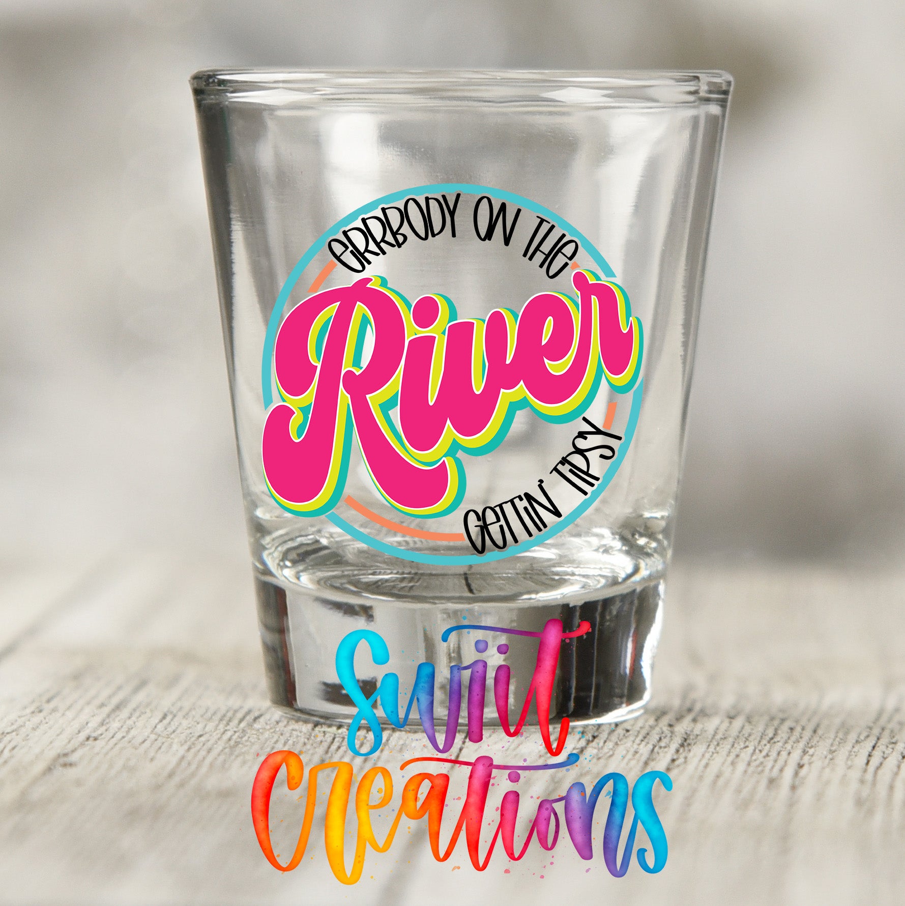 A shot glass with a colorful design and text on it, placed on a wooden surface.