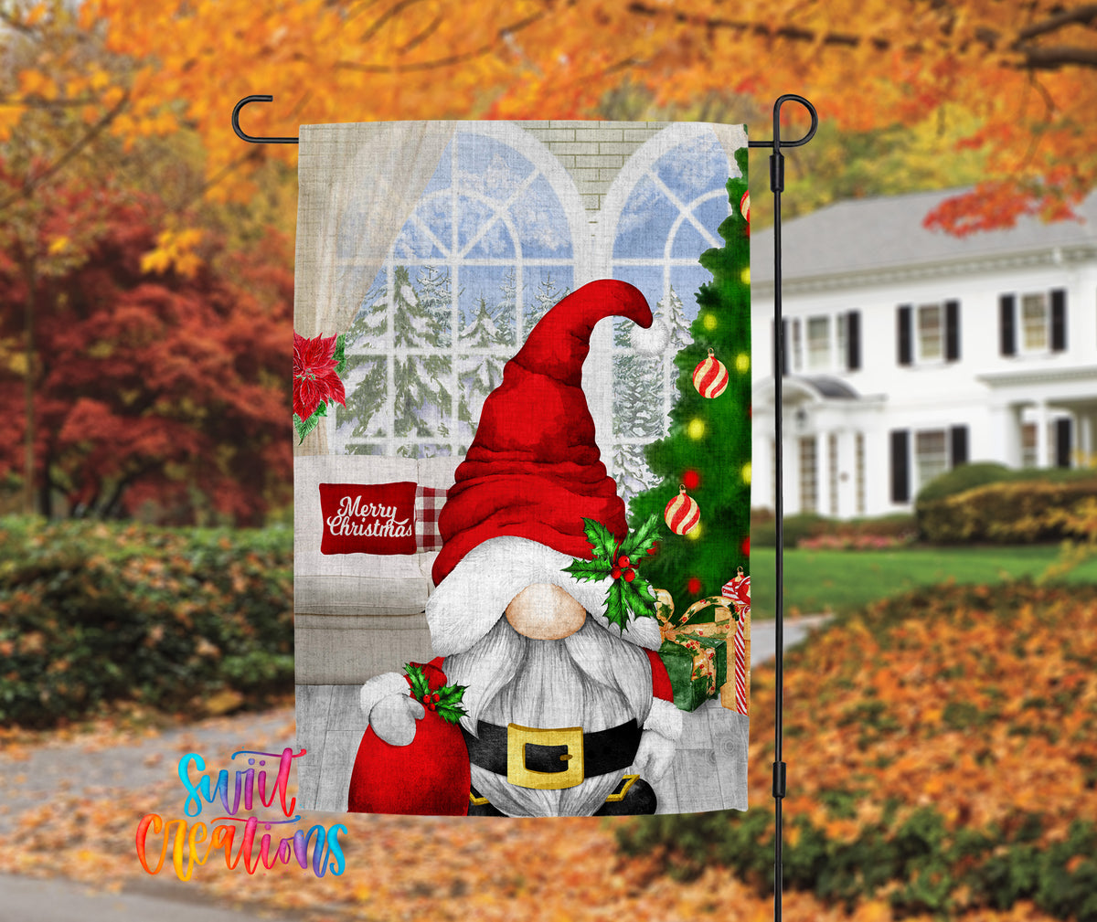 A Christmas-themed garden flag featuring a gnome wearing a Santa hat and holding a sack of presents, with a snowy landscape and a Christmas tree in the background.