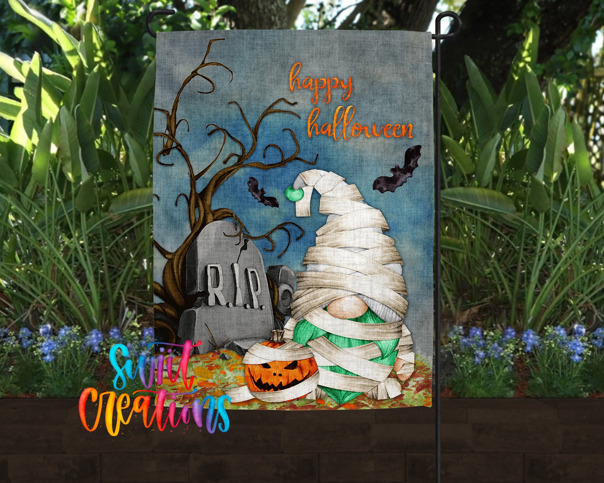 A Halloween-themed garden flag featuring a gnome wrapped in white cloth, a carved pumpkin, a gravestone, and bats flying overhead.