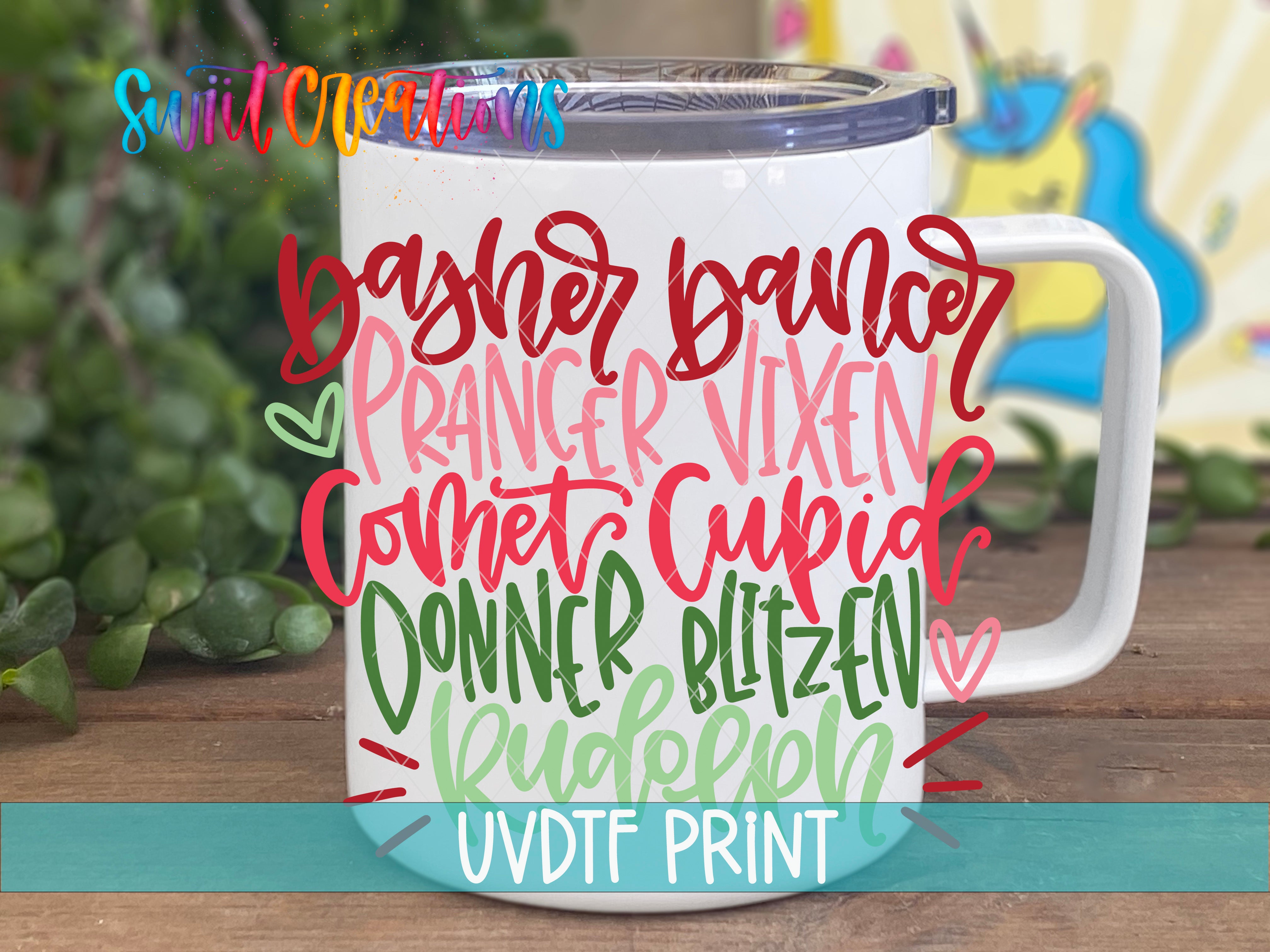 A white mug with colorful text printed on it, placed on a wooden surface with greenery in the background.