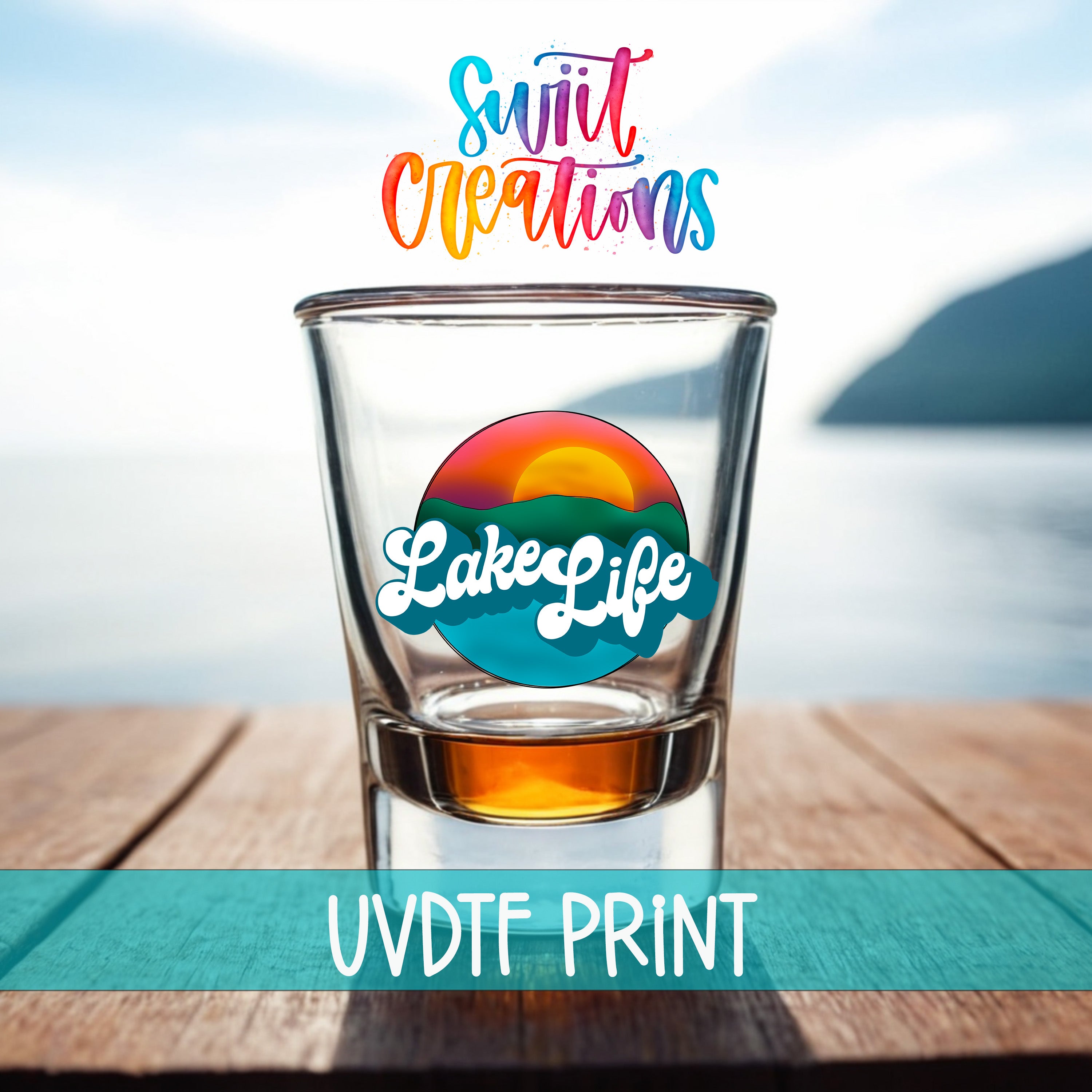A shot glass with a colorful design and text, placed on a wooden surface with a scenic background of a body of water and mountains.
