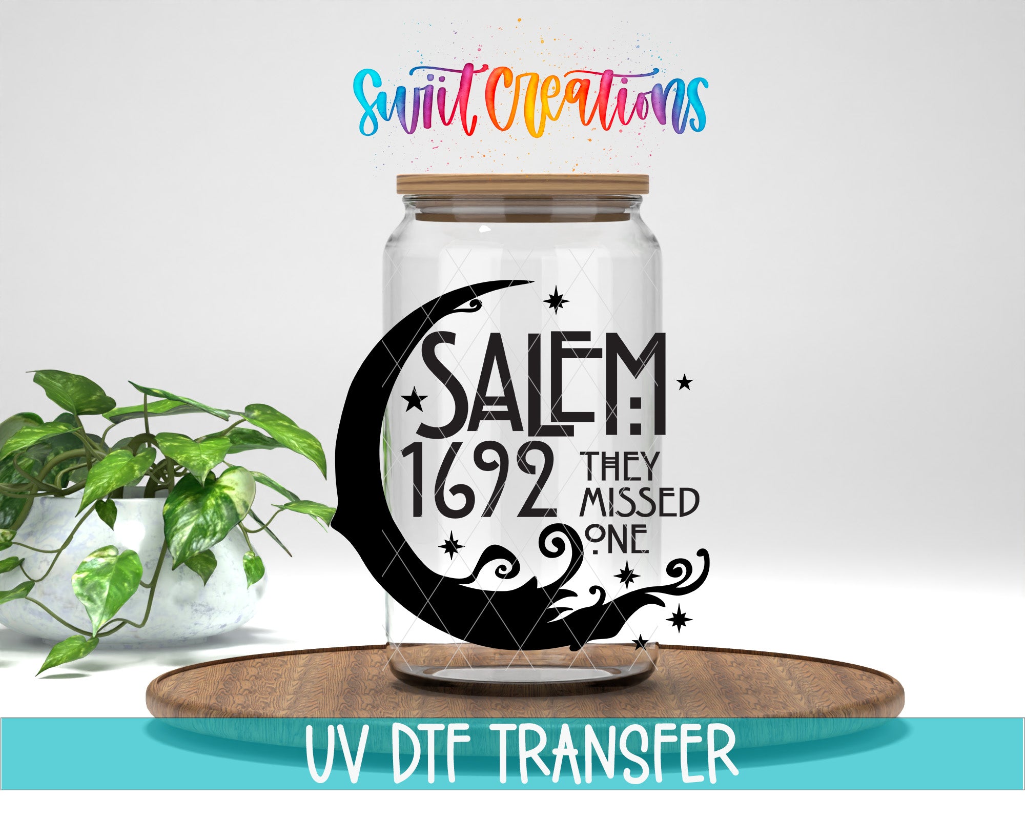 a glass jar with a crescent moon and stars design, along with the text "SALEM 1692 THEY MISSED ONE" printed on it. The jar is placed on a wooden surface, and there is a potted plant in the background.