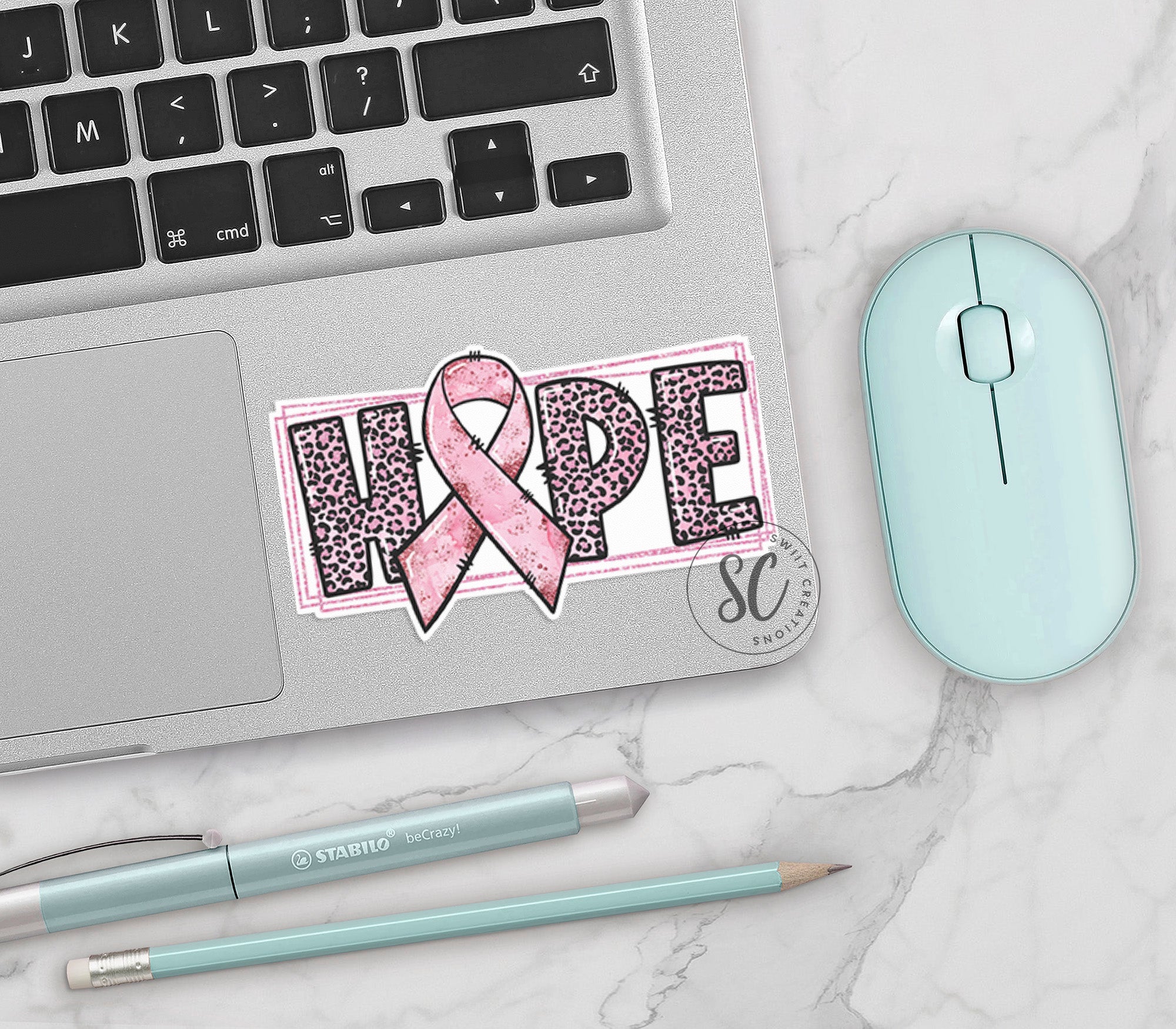 a pink ribbon sticker on a laptop next to a mouse
