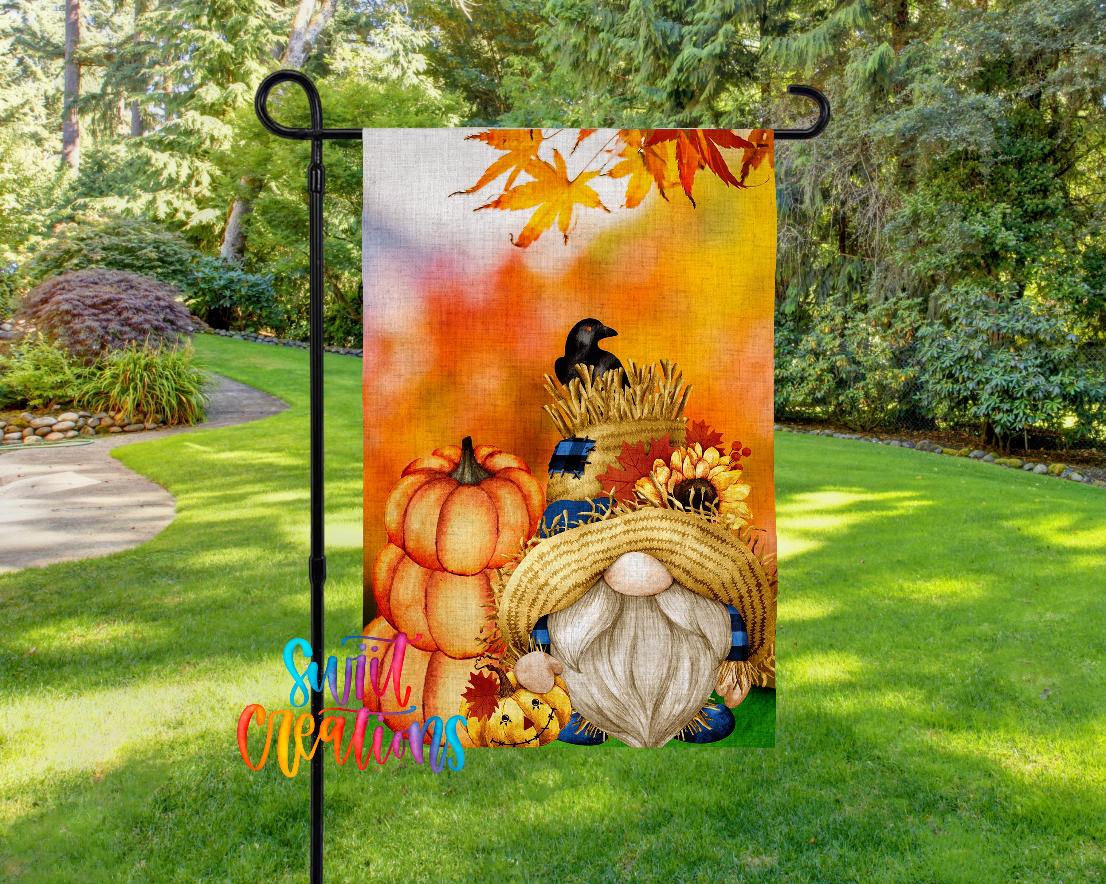 A colorful autumn-themed garden gnome flag is displayed on a metal pole in a lush, green garden setting.