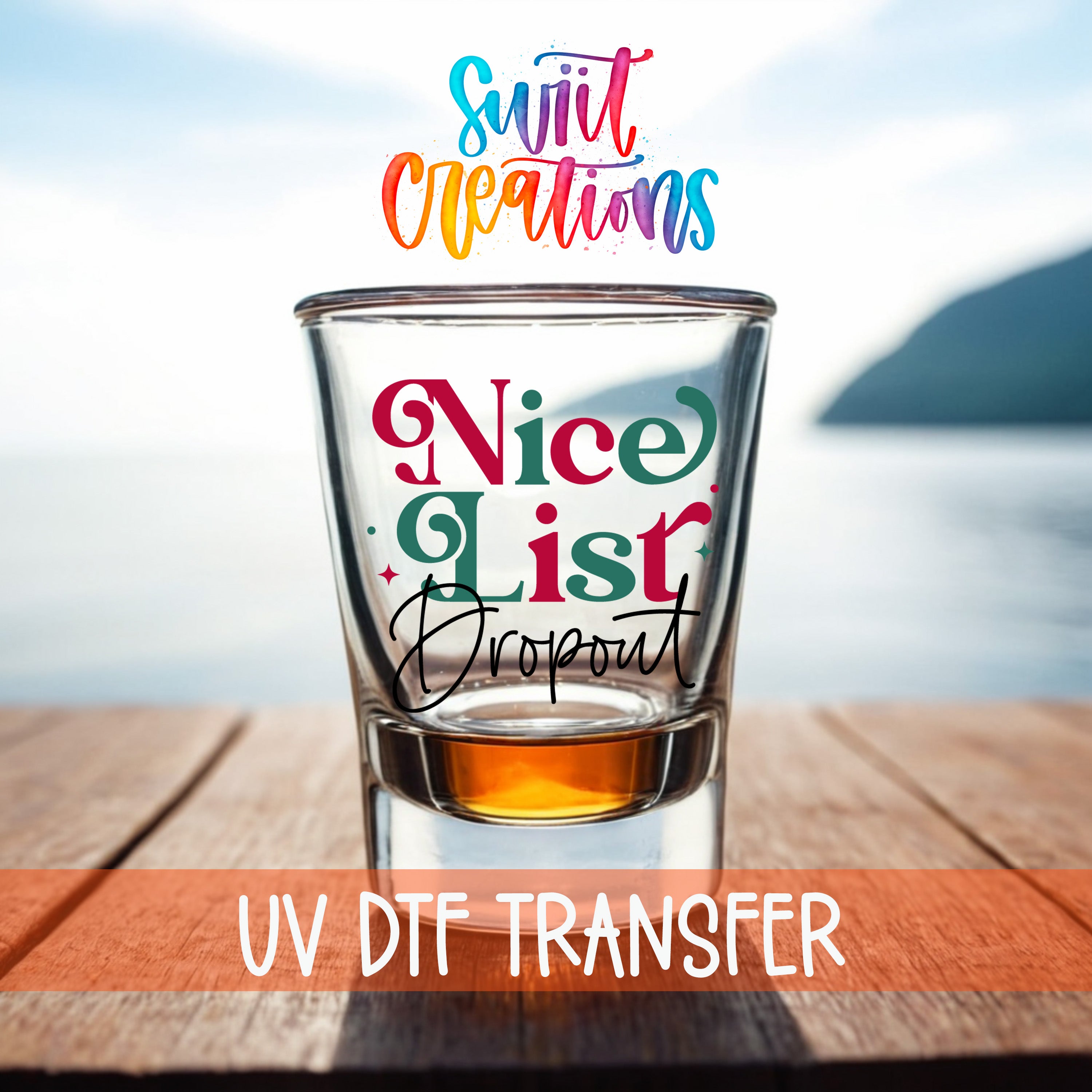 a shot glass with a colorful design and text, placed on a wooden surface with a body of water in the background.