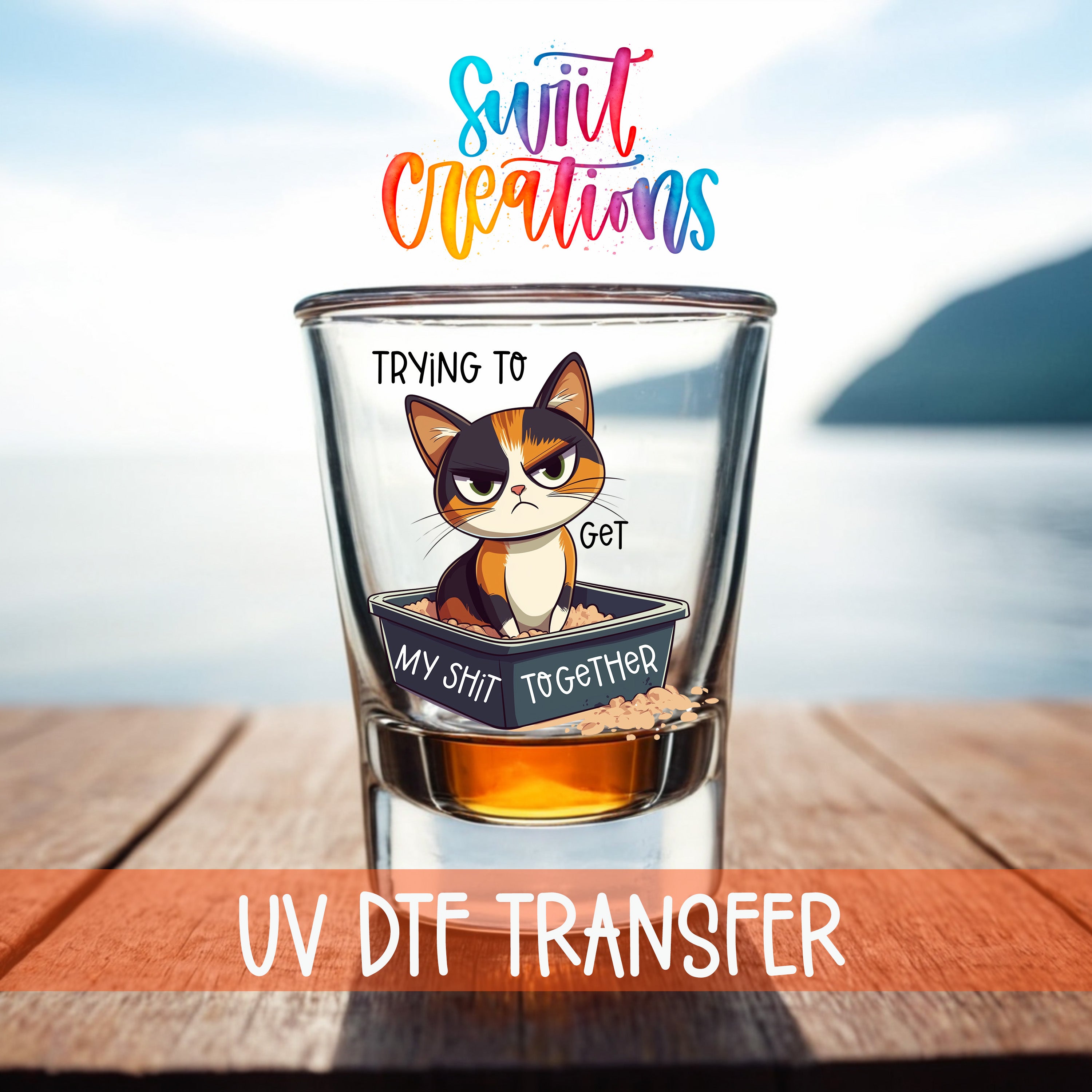 A glass with a cartoon cat illustration and text, placed on a wooden surface with a body of water in the background.
